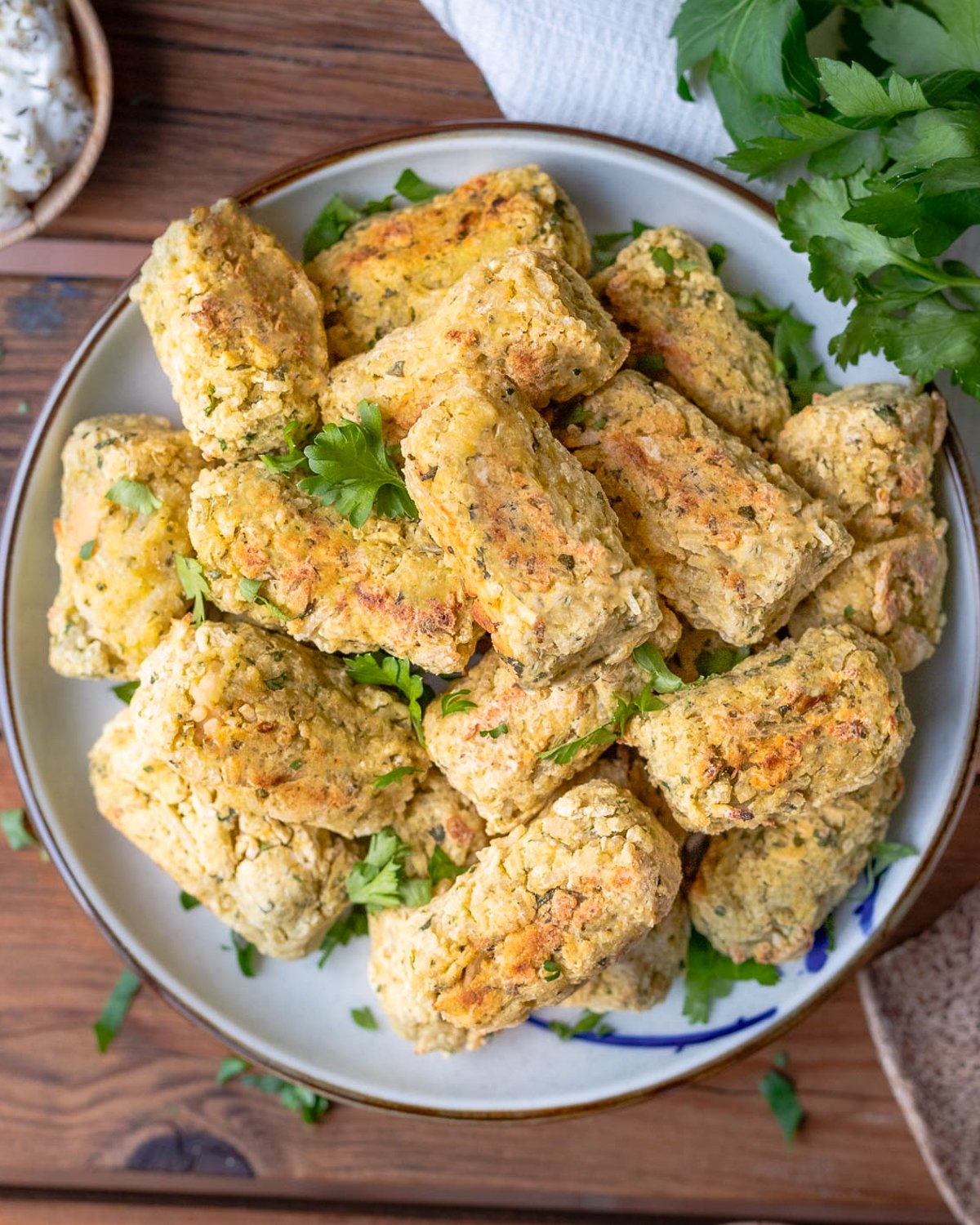 A plate of brazilian rice balls that have been baked until golden brown and topped with fresh parsley.