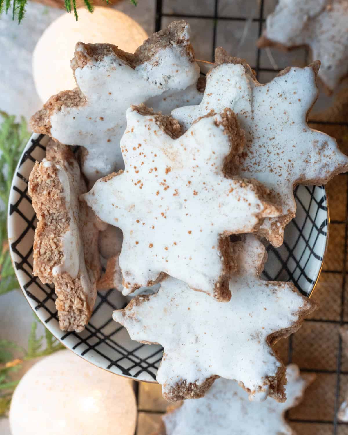 Vegan Zimtsterne cookies nestled in a black basket, showing off the white icing and cinnamon sprinkle, with a warm and cozy Christmas ambiance in the background.