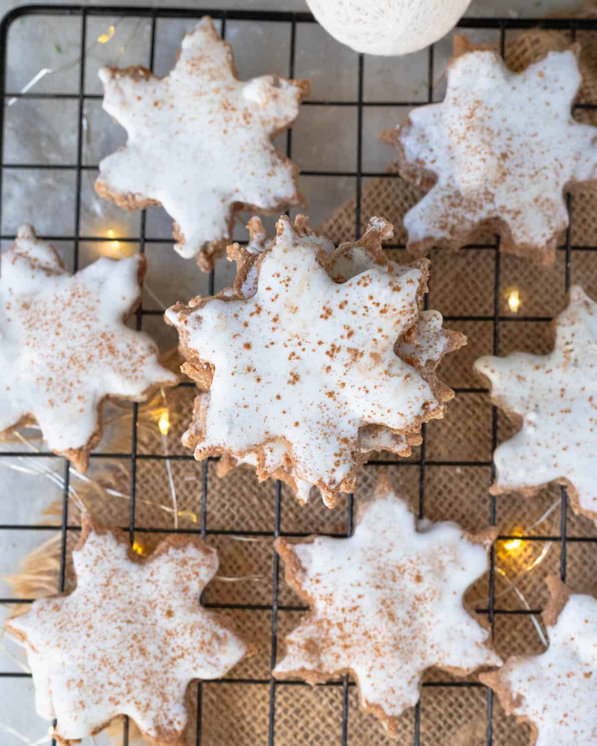 A close-up of the vegan Zimtsterne cookies, focusing on the texture and white glaze, with a sprinkle of cinnamon adding a touch of Swiss Christmas charm.
