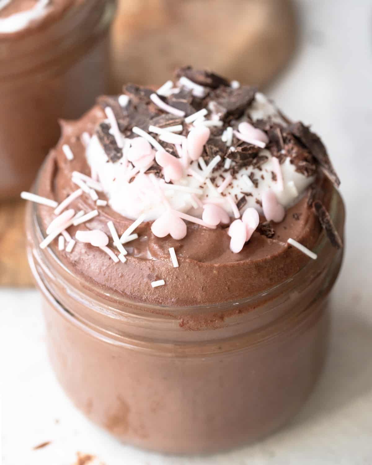 High Protein Chocolate Mousse in a glass jar, sprinkled with white and pink heart-shaped sprinkles and chocolate shavings for a festive touch.