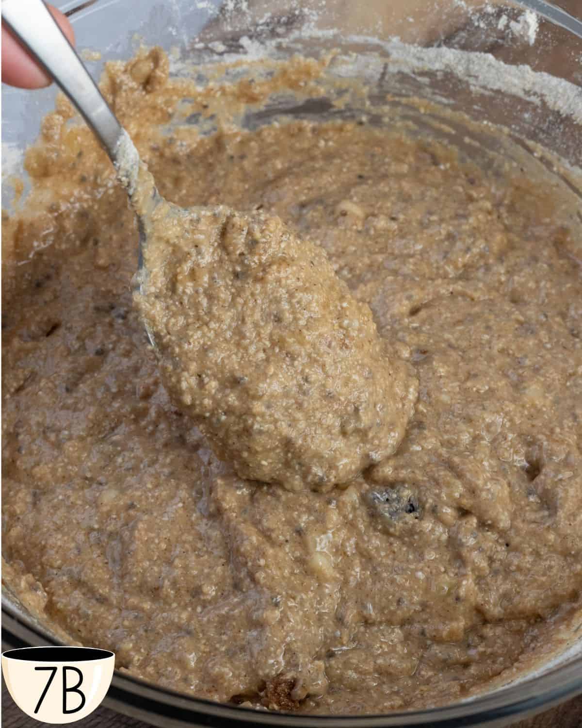 Hand scooping a spoonful of oatmeal muffin batter, showcasing the texture before adding fruit.