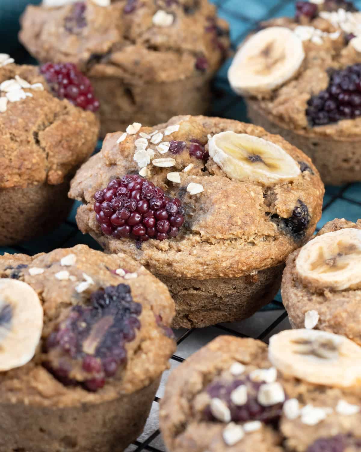 Homemade oatmeal muffins studded with blackberries and banana pieces on a cooling rack, sprinkled with oats.