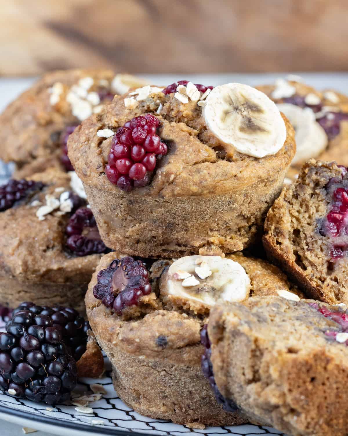Oatmeal muffins with vibrant blackberries and banana slices on top, showcased on a light-colored plate with a rustic backdrop.