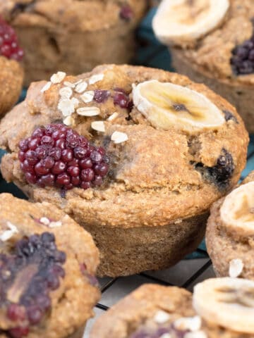 Gluten free blackberry muffins topped with fresh blackberries and banana slices, garnished with oat flakes.