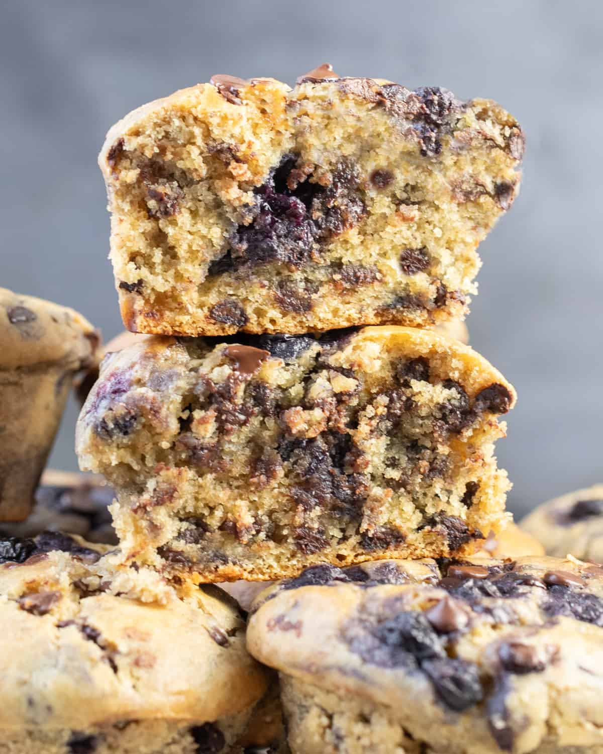 A muffin broken in half to showcase the moist interior with blueberries and chocolate chips, surrounded by whole muffins.