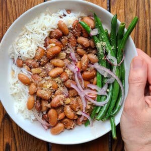 A complete meal showcasing Brazilian pinto beans served over Brazilian rice with a side of green beans, exemplifying a traditional Brazilian rice and beans dish.