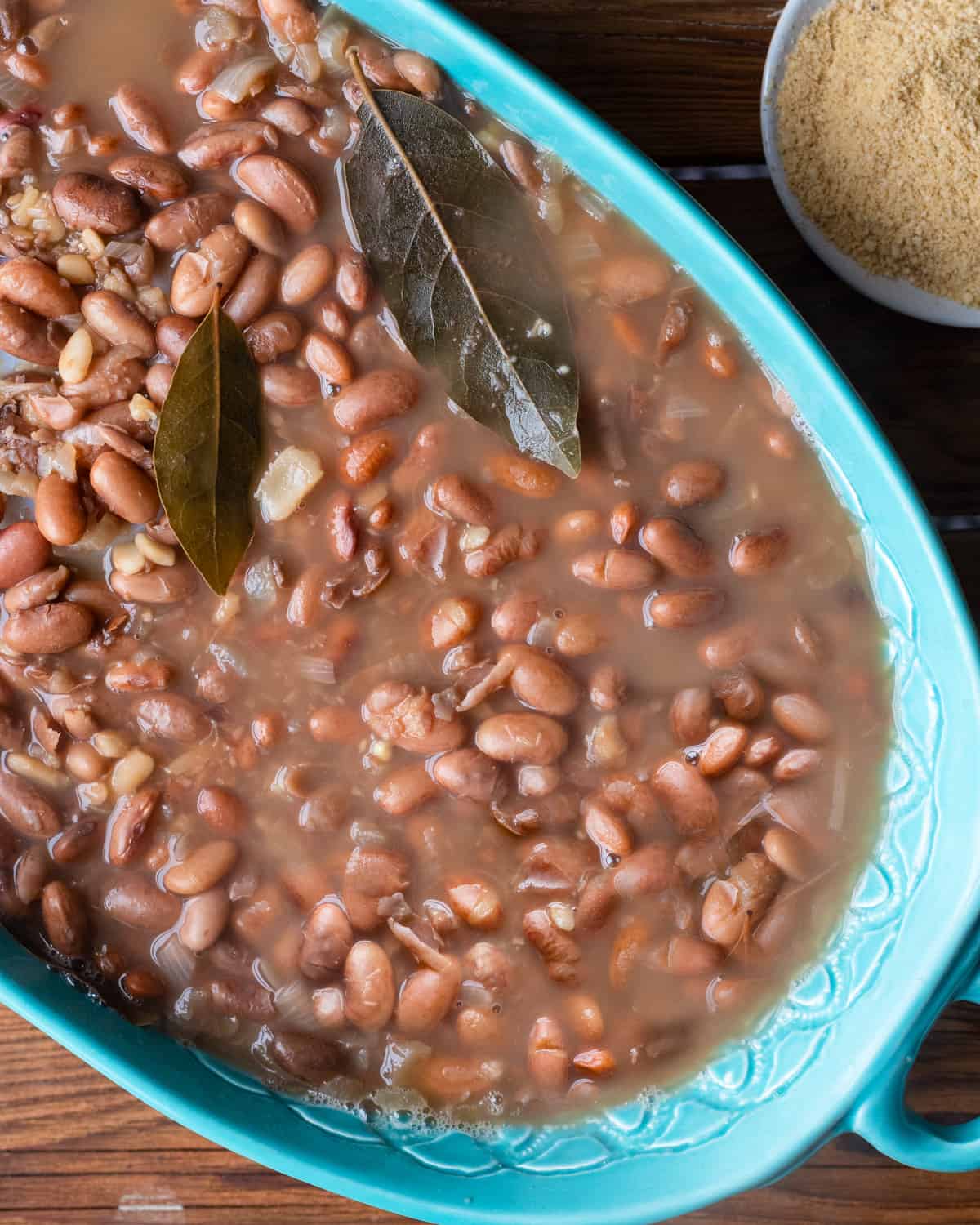 A close-up image showing a traditional Brazilian pinto beans stew with two bay leaves visible, suggesting a hearty and aromatic dish.