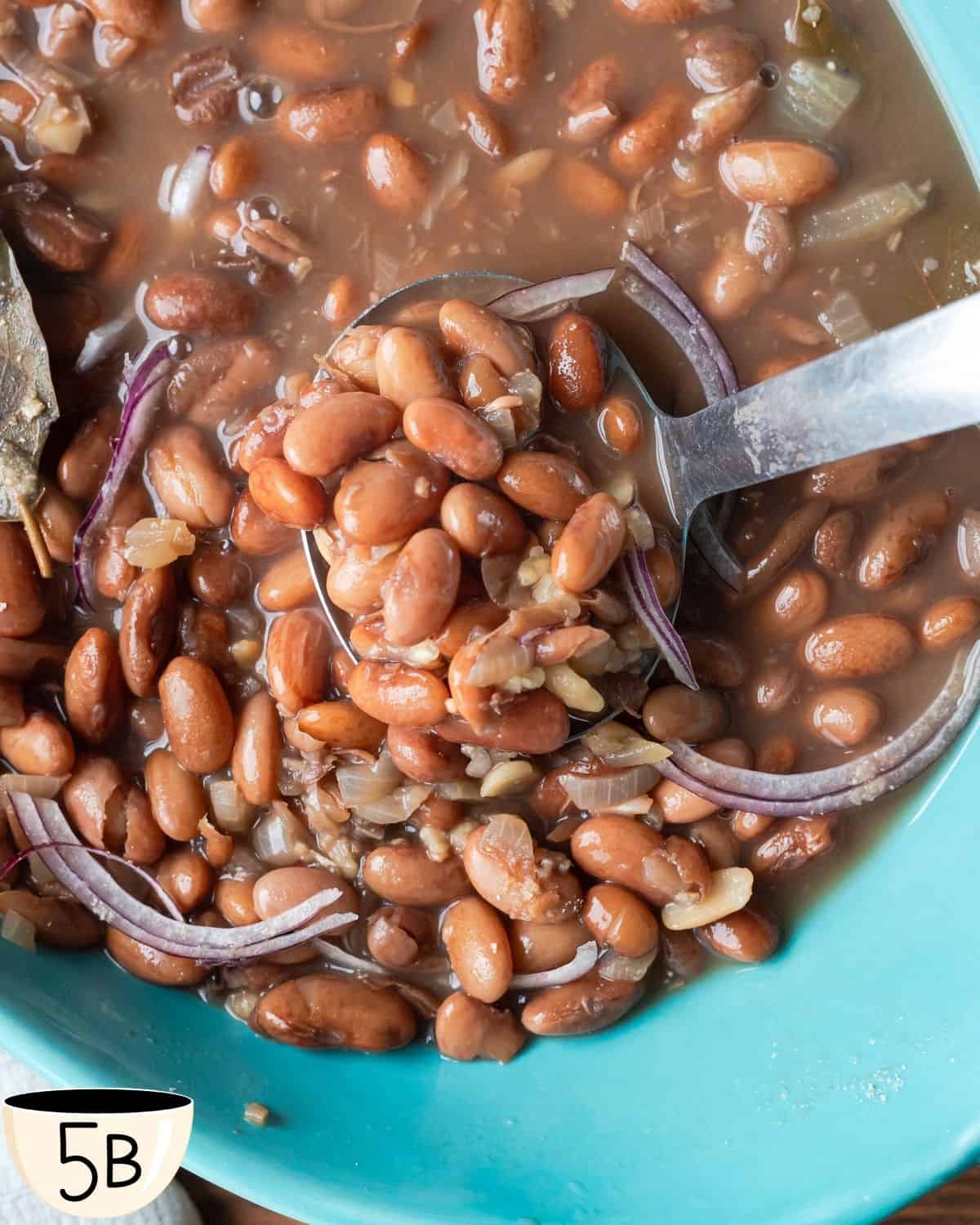 A close-up of a ladle filled with Brazilian pinto beans and onions in a rich, savory broth, ready to be served.