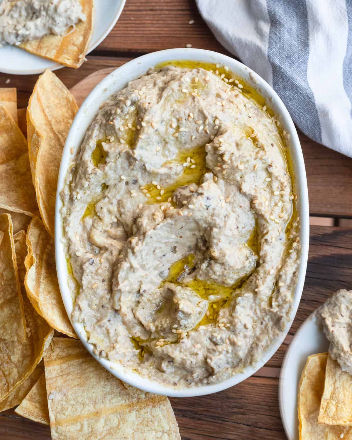 An inviting bowl of baba ganoush with a rich drizzle of olive oil and sesame seeds, served with pita chips, on a rustic wooden table.