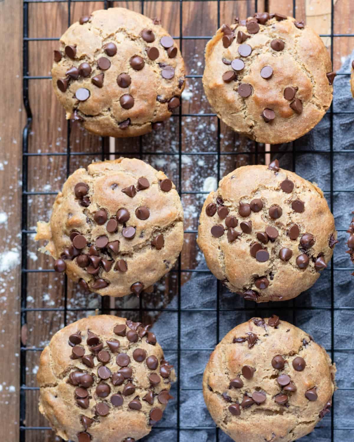 A top-down view of freshly baked gluten-free chocolate chip muffins cooling on a wire rack, scattered with additional chocolate chips.