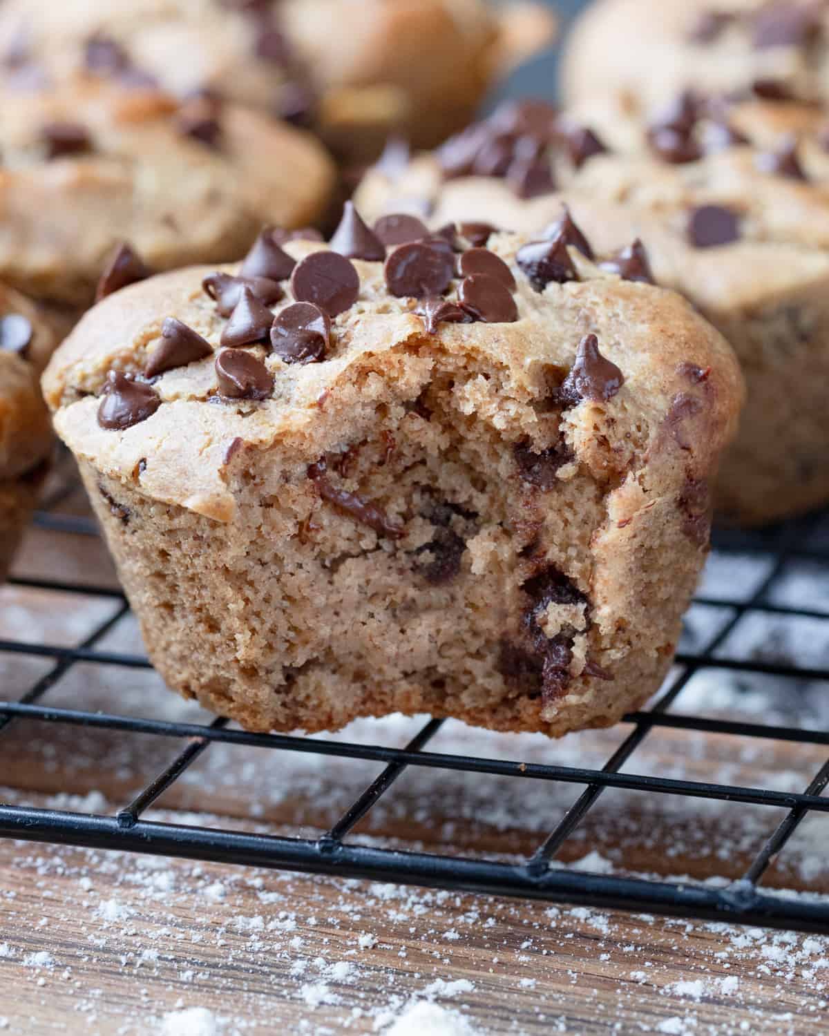 A close-up of a gluten-free chocolate chip muffin with a section removed, showing the dense and moist crumb texture with chocolate chips.