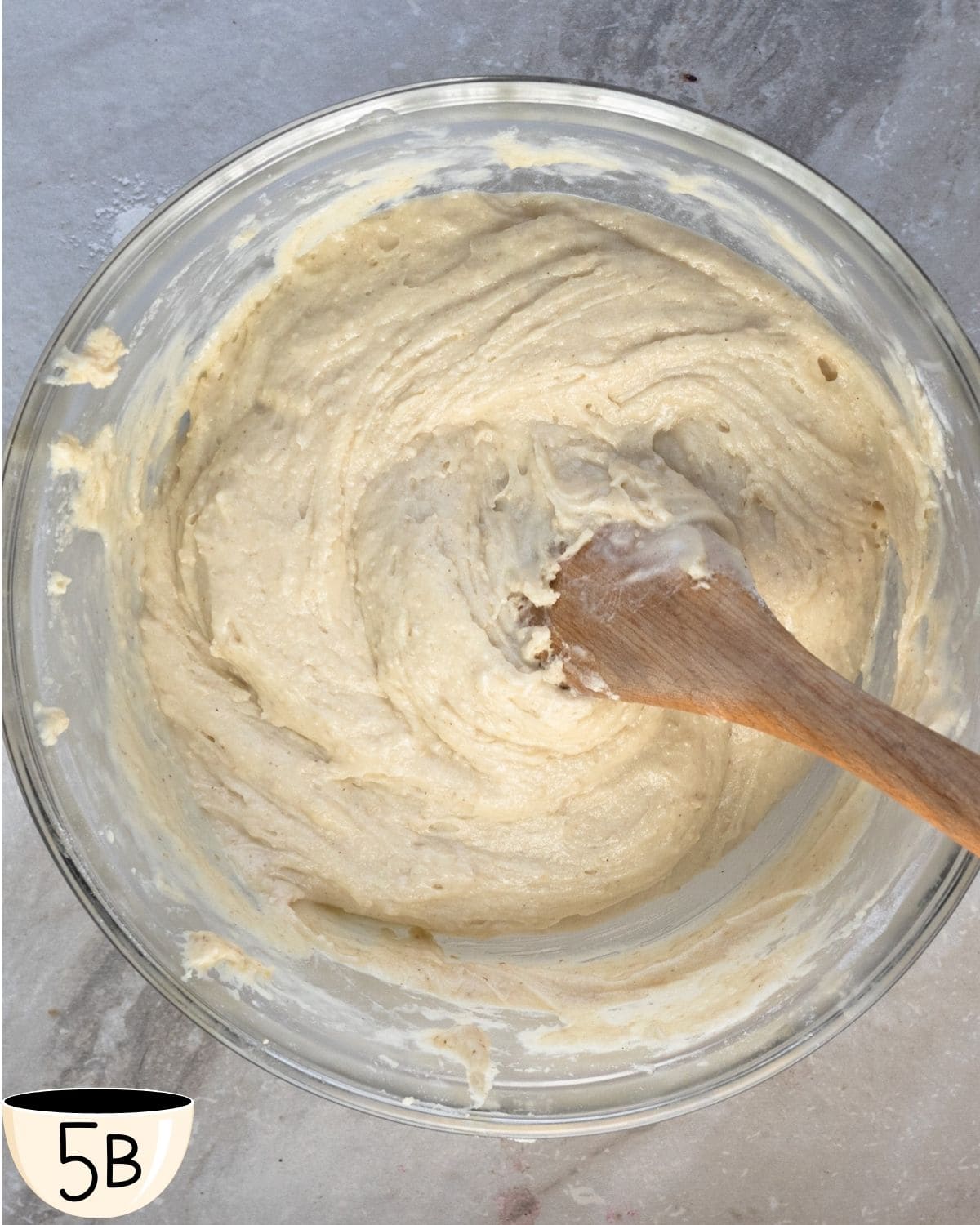 Gluten free chocolate chip muffin batter in the glass bowl after being mixed, showing a smooth, creamy consistency with the wooden spoon still in the bowl.