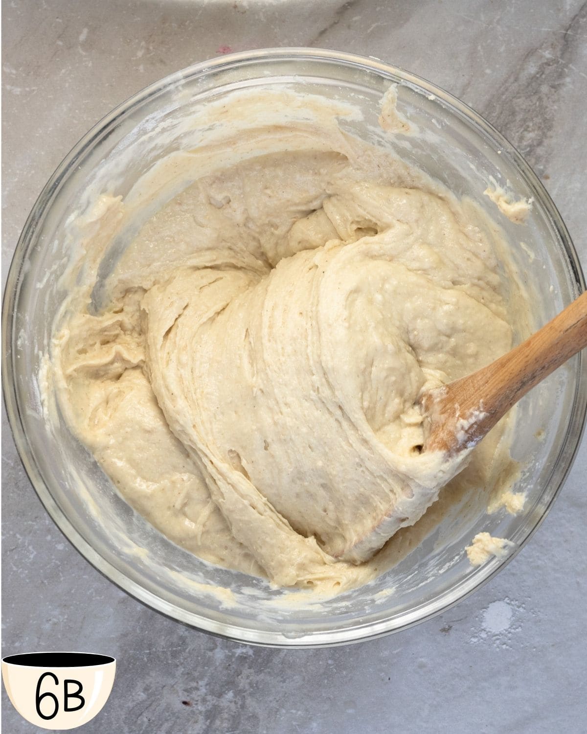 The gluten-free muffin batter fully mixed and rested to show the consistency of the batter and that it is ready for the addition of chocolate chips, with the wooden spoon resting in the bowl.