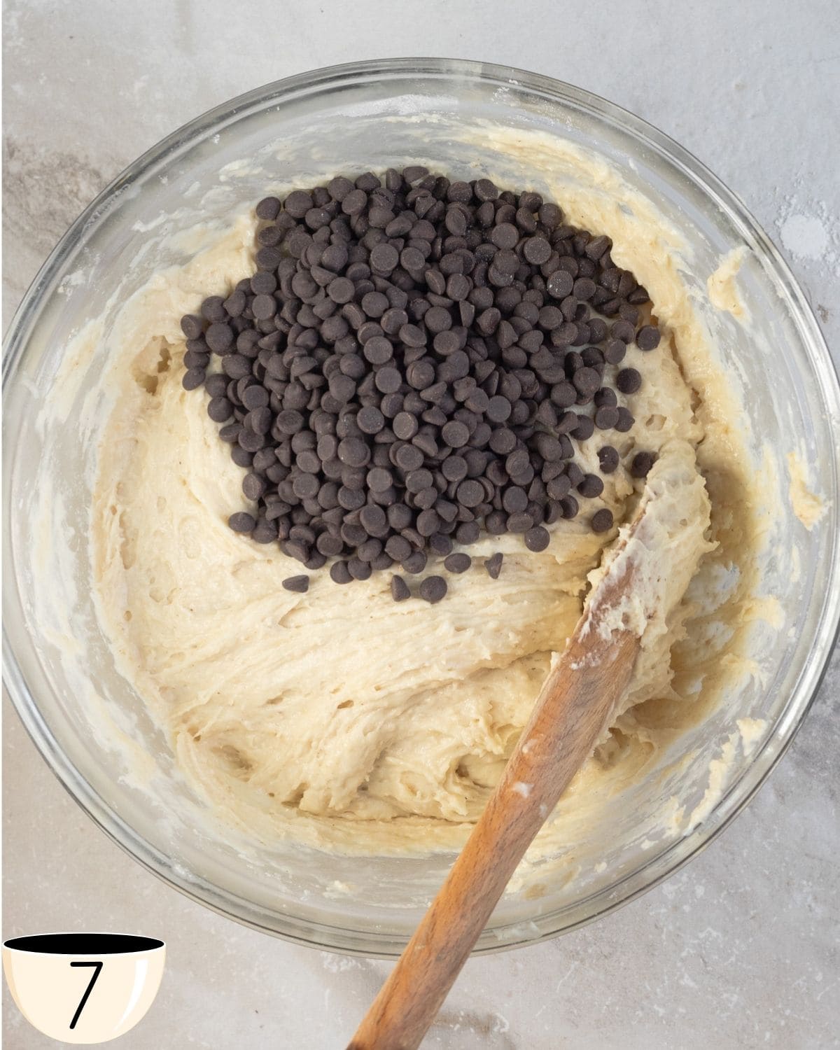 A heap of chocolate chips poured onto the center of the gluten-free muffin batter in the glass bowl.