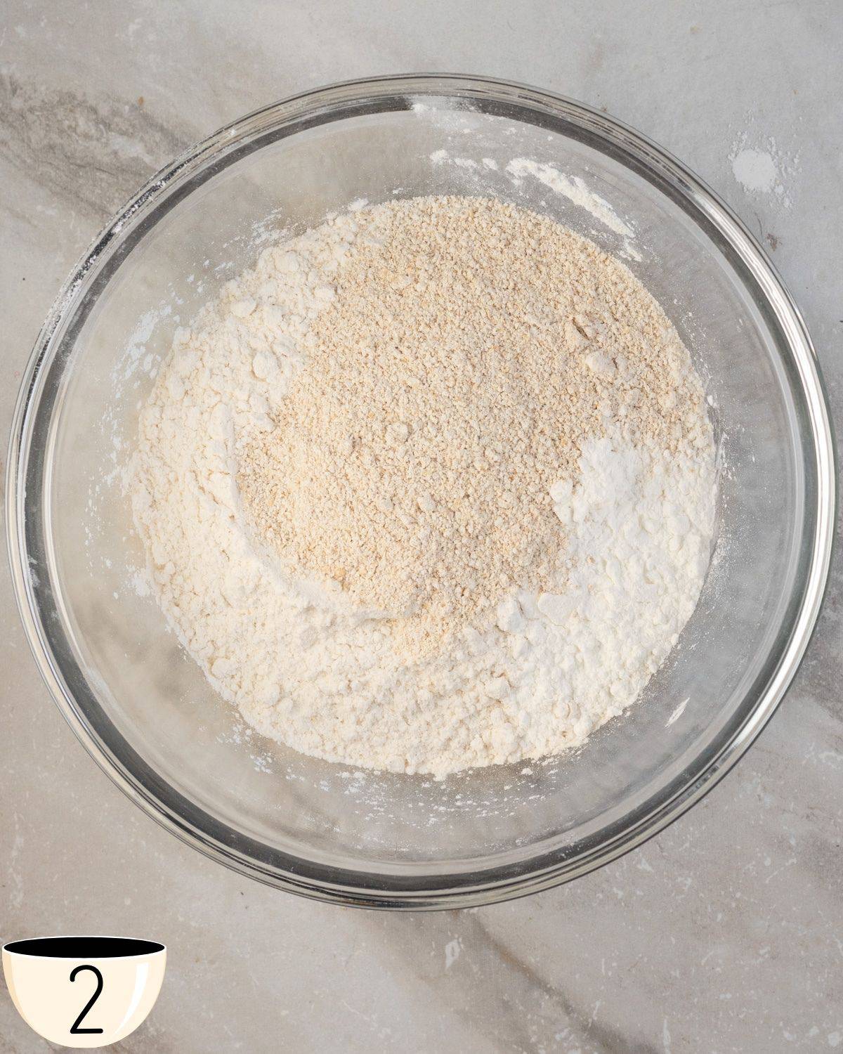A large glass bowl containing a blend of oat flour and gluten-free all-purpose flour on a marble kitchen surface.