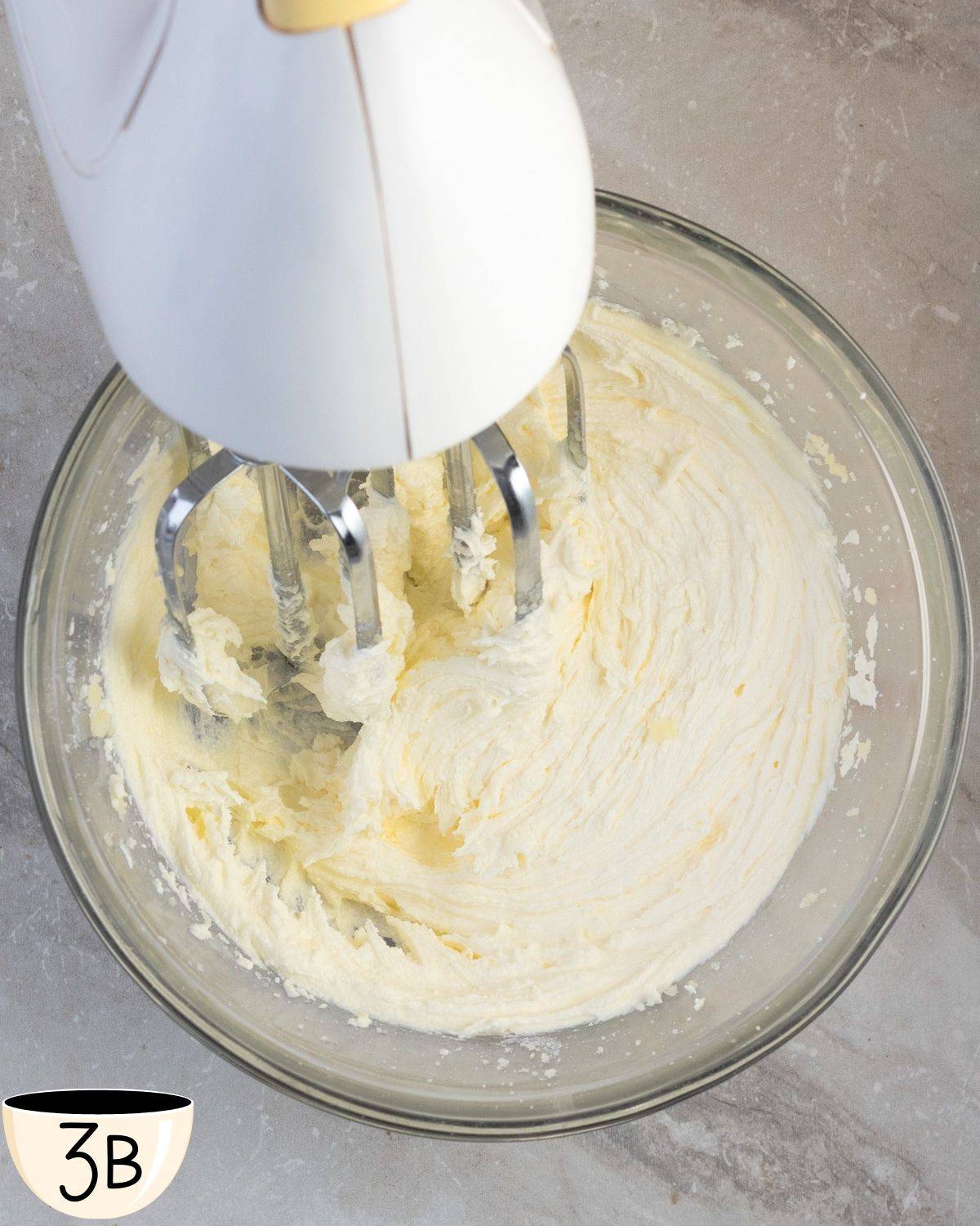 A creamy mixture of butter and sugar in a glass bowl after being whipped to a smooth consistency