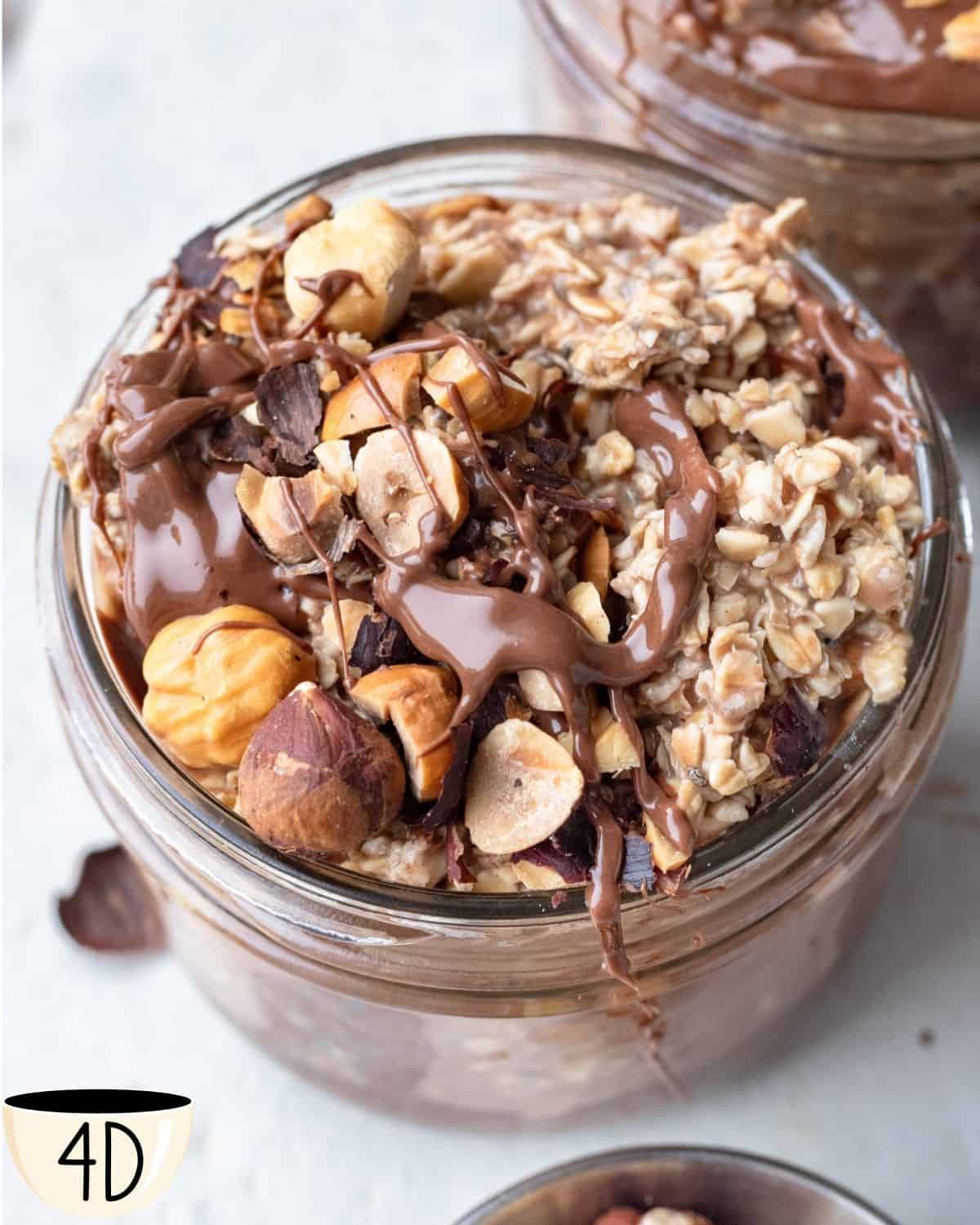 A jar of overnight oats with Nutella, generously topped with whole hazelnuts, banana slices, and a drizzle of chocolate.