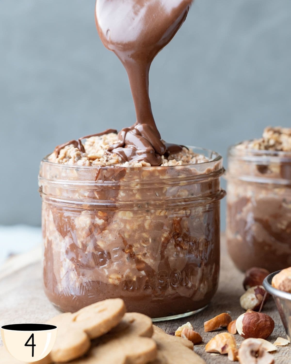 Pouring creamy Nutella onto a jar of overnight oats with hazelnuts, creating a luscious layer on top.