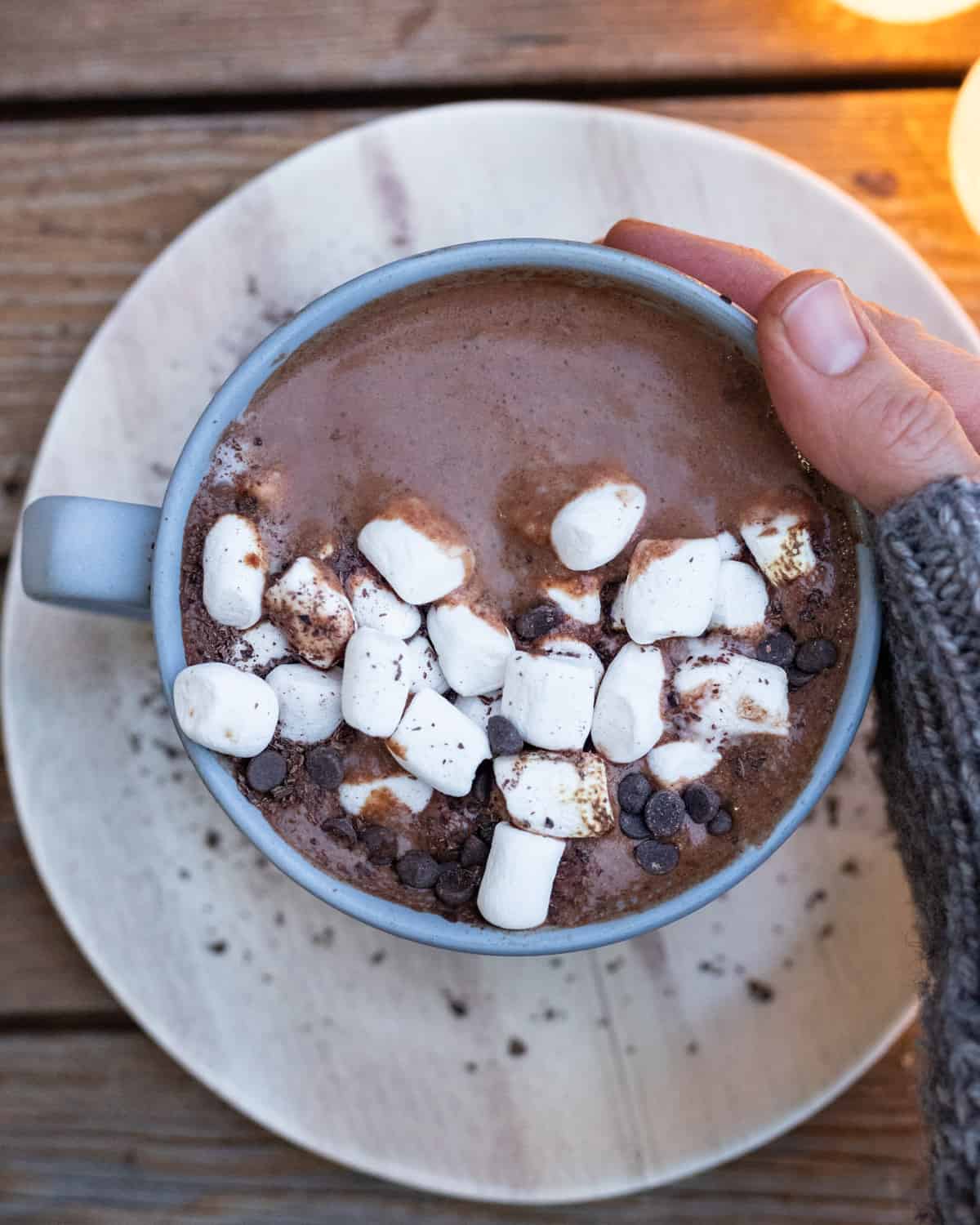 A delicious cup of hot chocolate with marshmallows and chocolate chips, perfect for a cold day, presented on a white plate with a wooden backdrop.