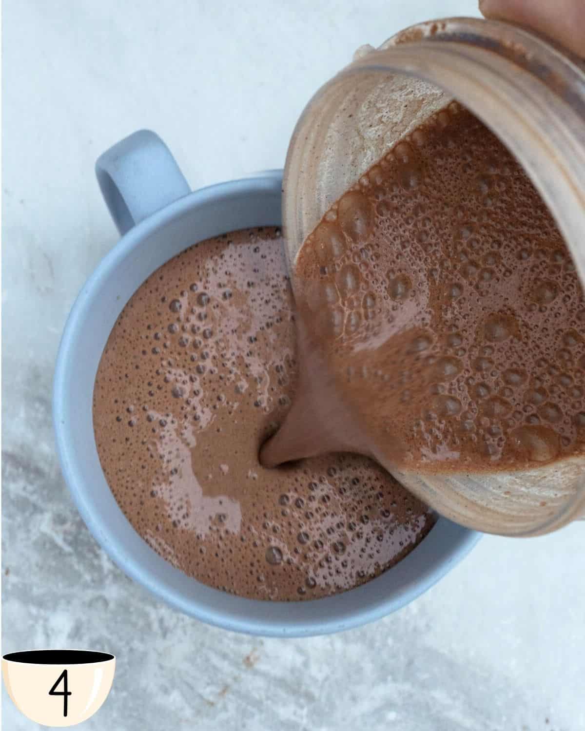 Hot chocolate with protein being poured into a mug ready to drink. The warm beverage is creamy and smooth.