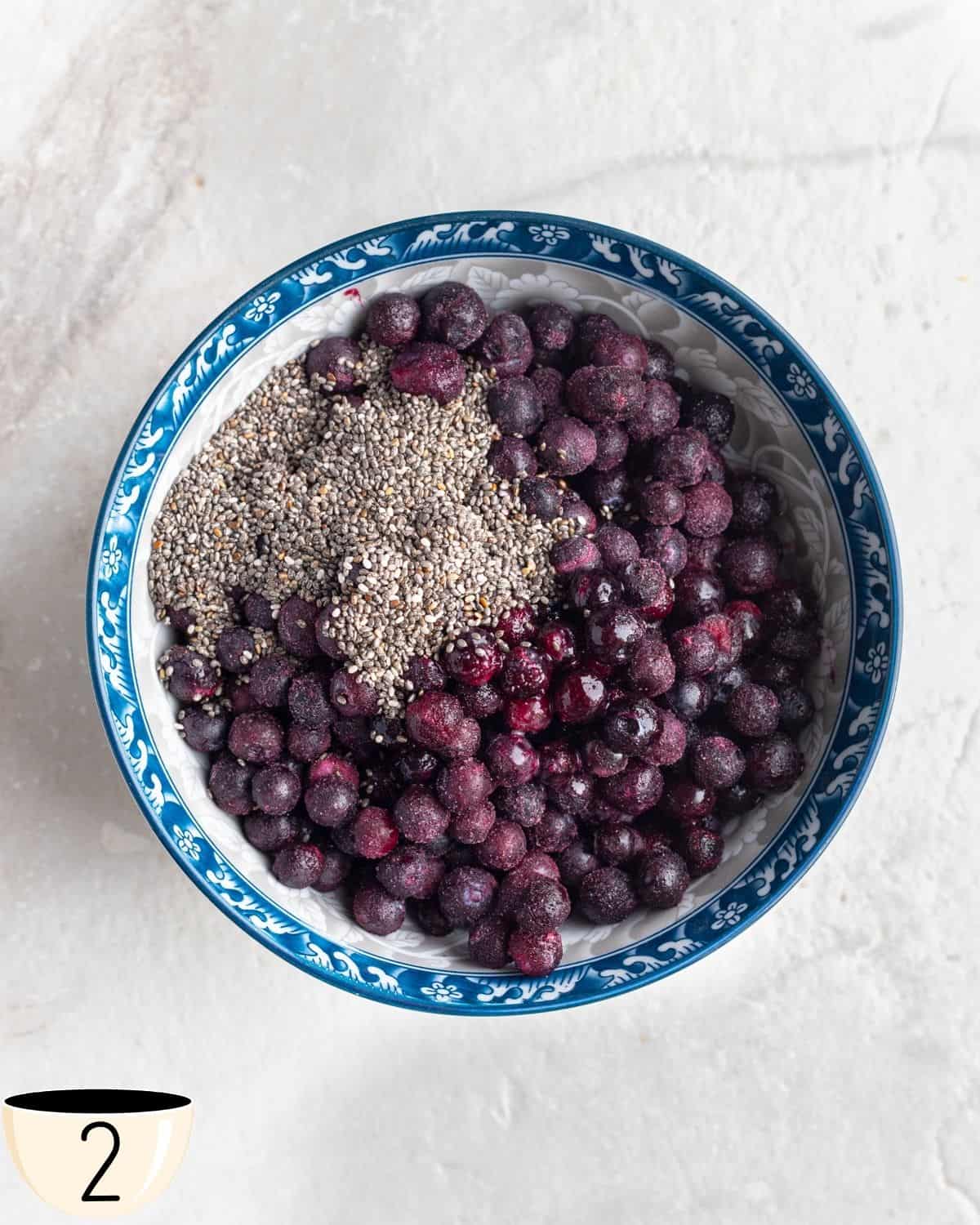 A bowl of frozen blueberries topped with chia seeds, in preparation to be microwaved to make a compote layer for overnight oats.