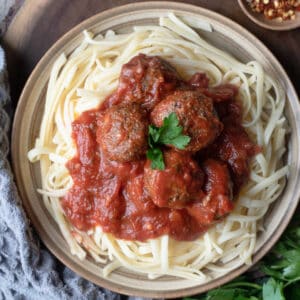 Plate of gluten free pasta topped with vegan meatballs in a tomato sauce.