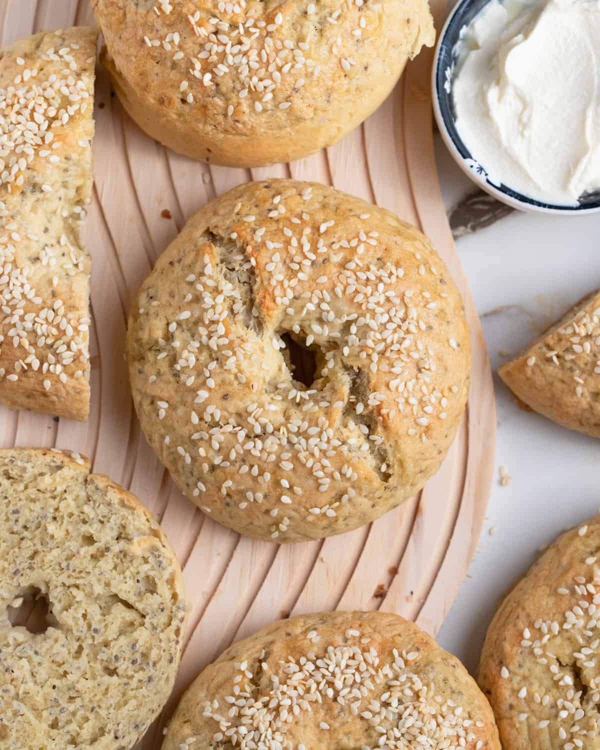 Overhead shot of gluten-free vegan bagels with sesame seeds, alongside a dish of vegan cream cheese.