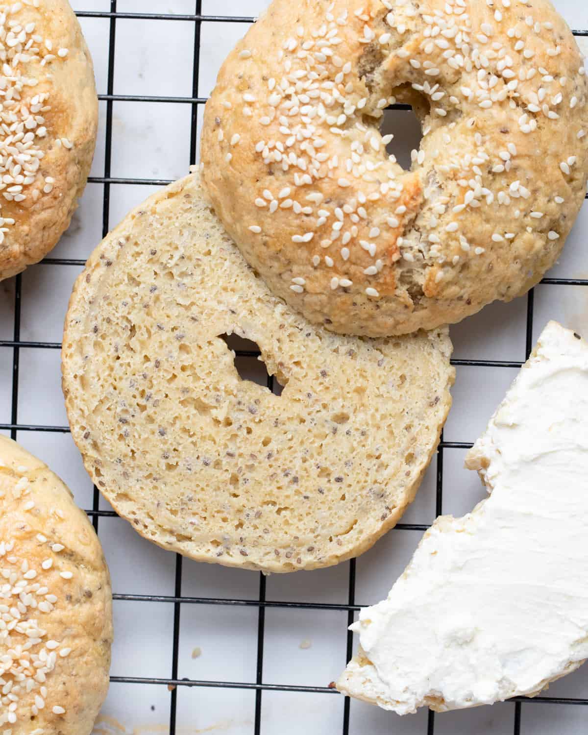 A single gluten-free vegan bagel with sesame seeds on a black plate, with a side of cream cheese.