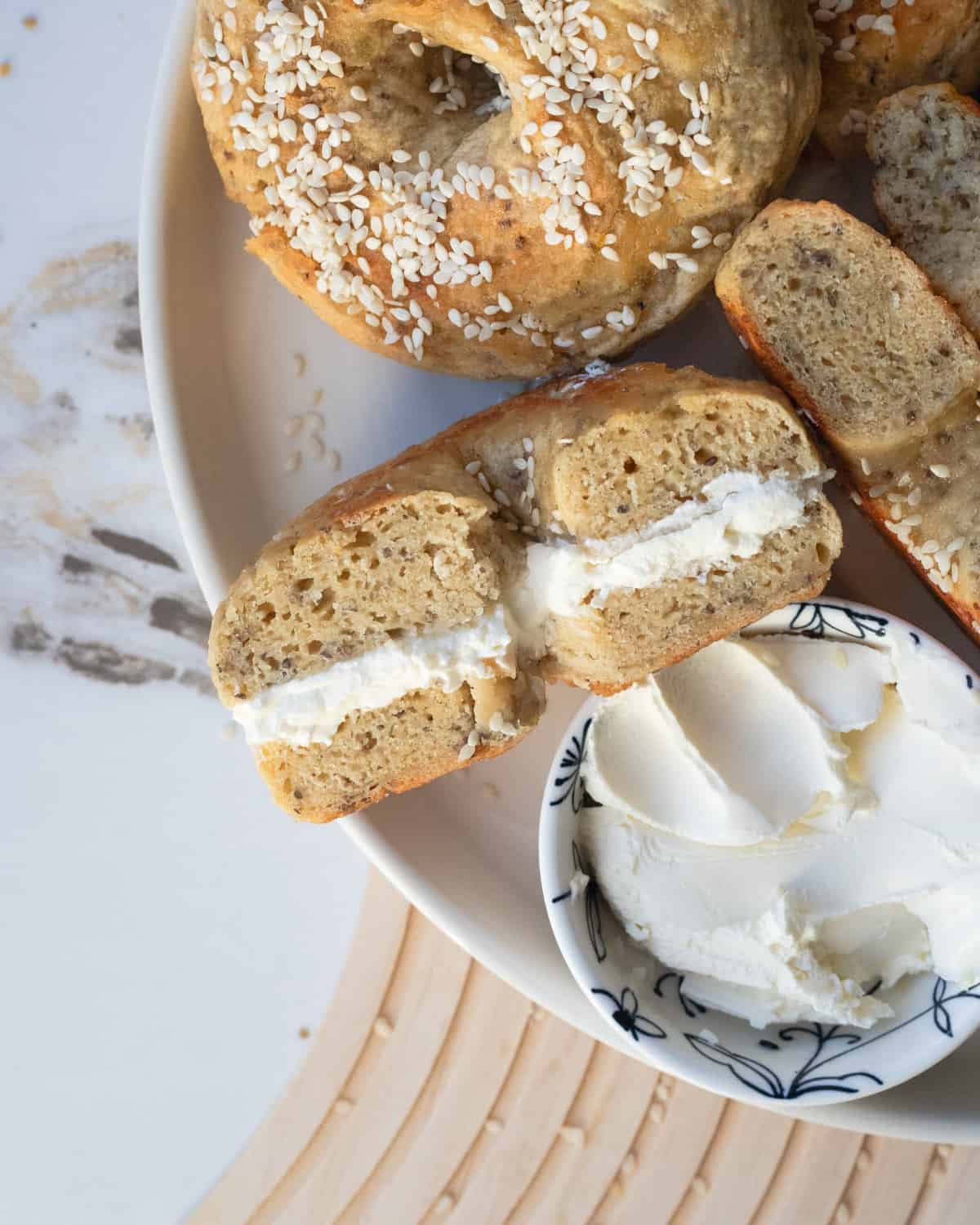 A bagel sliced in half with cream cheese on one side, displayed on a wire cooling rack.