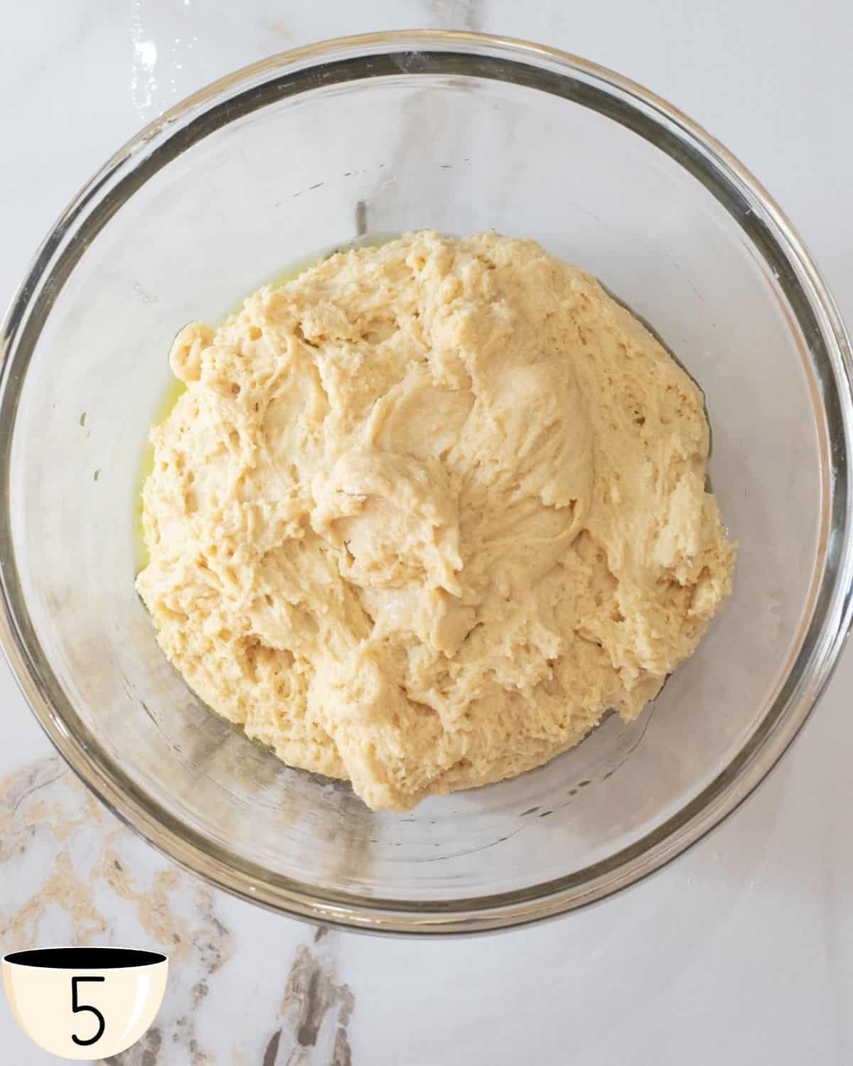 Dough in a bowl after initial mixing, with a smooth top surface, indicating readiness for the rising process in gluten-free bagel making.