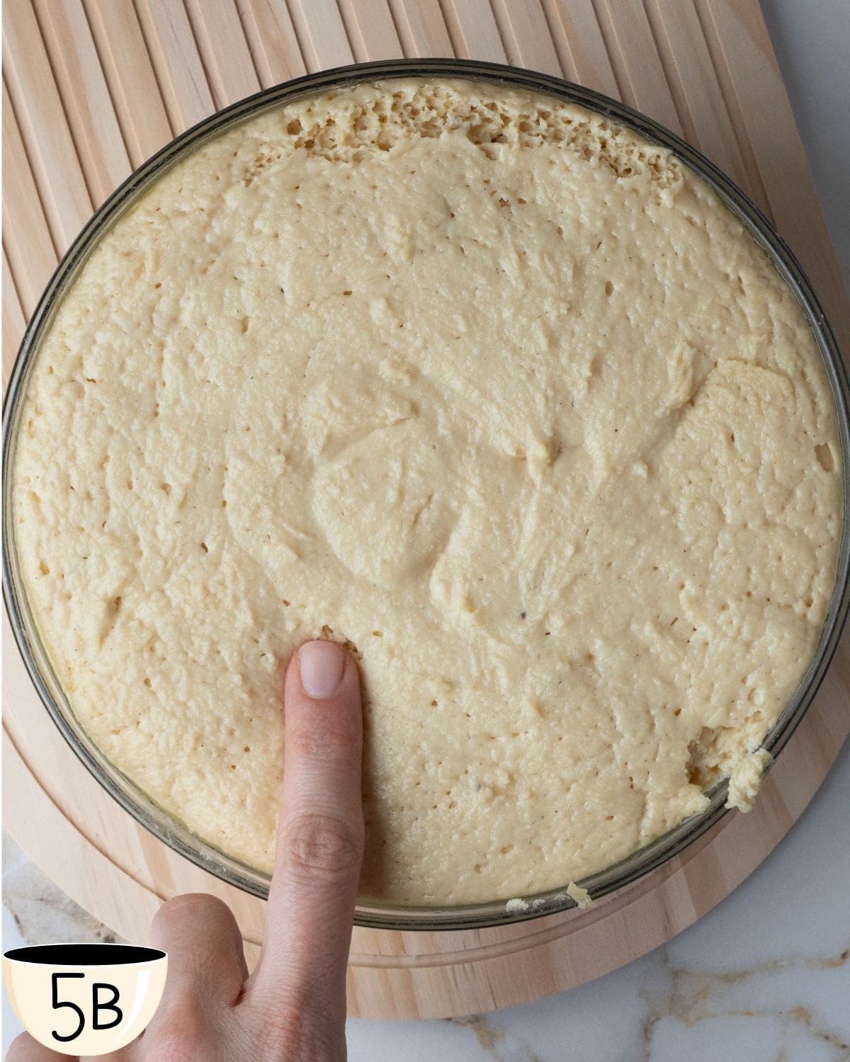 A person's finger presses into the dough to test its rise, an essential step in ensuring proper fermentation for gluten-free bagels.