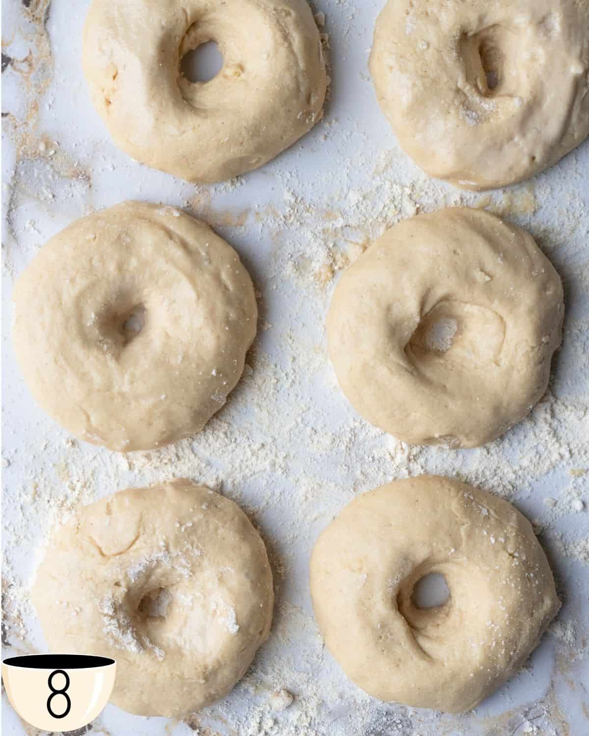 Six gluten-free bagel dough portions shaped into rings with center holes on a floured surface.