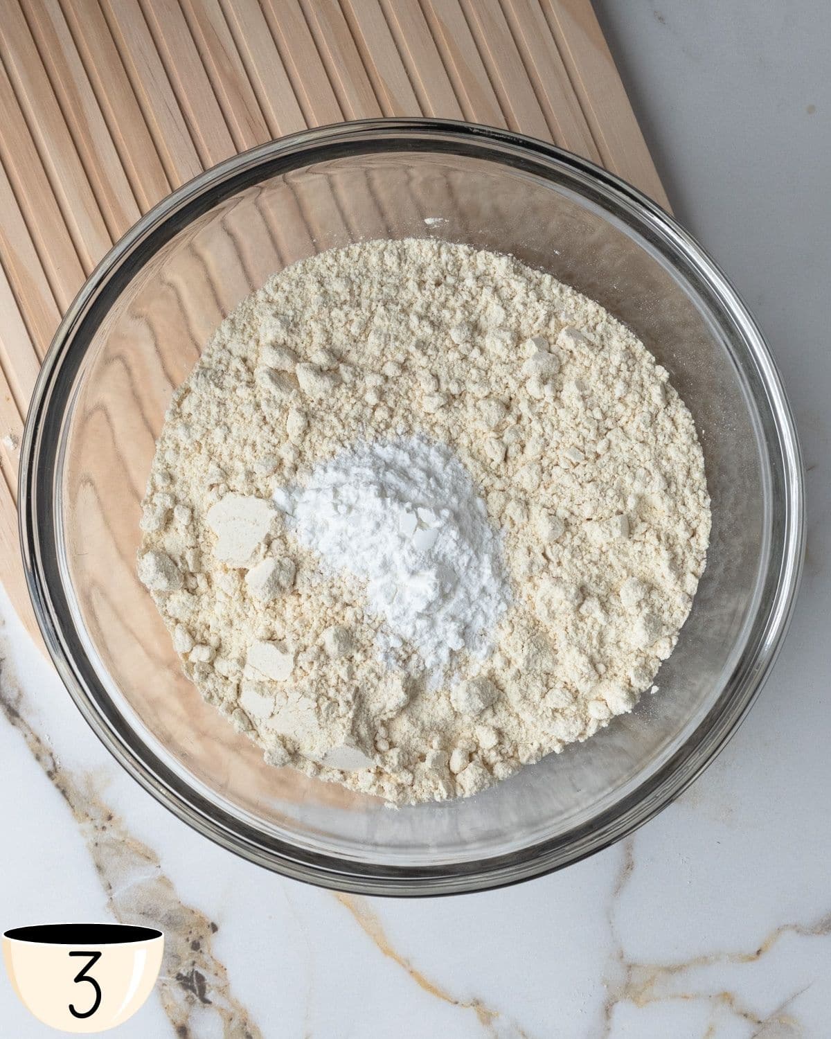 A clear glass bowl containing gluten-free all-purpose flour, baking powder, and salt ready for mixing.