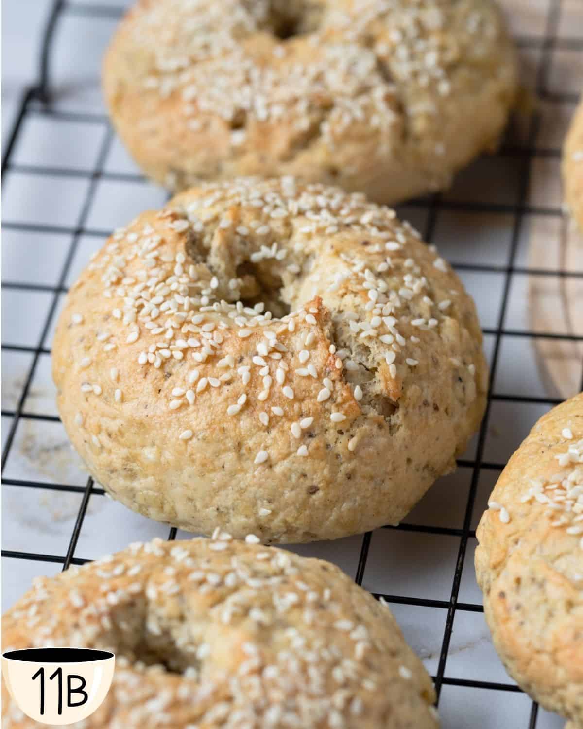 Close-up of freshly baked gluten-free vegan bagels topped with sesame seeds, cooling on a wire rack.