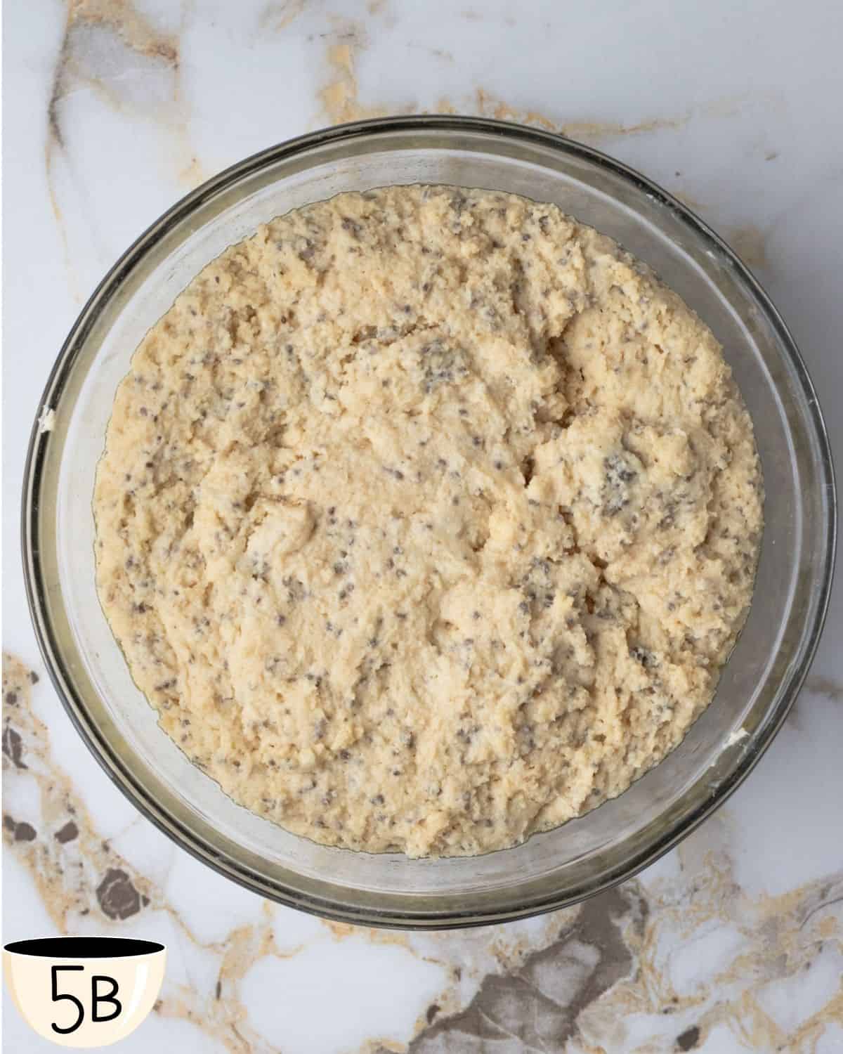 Gluten-free vegan bagel dough after rising, shown in a glass bowl on a marble countertop.