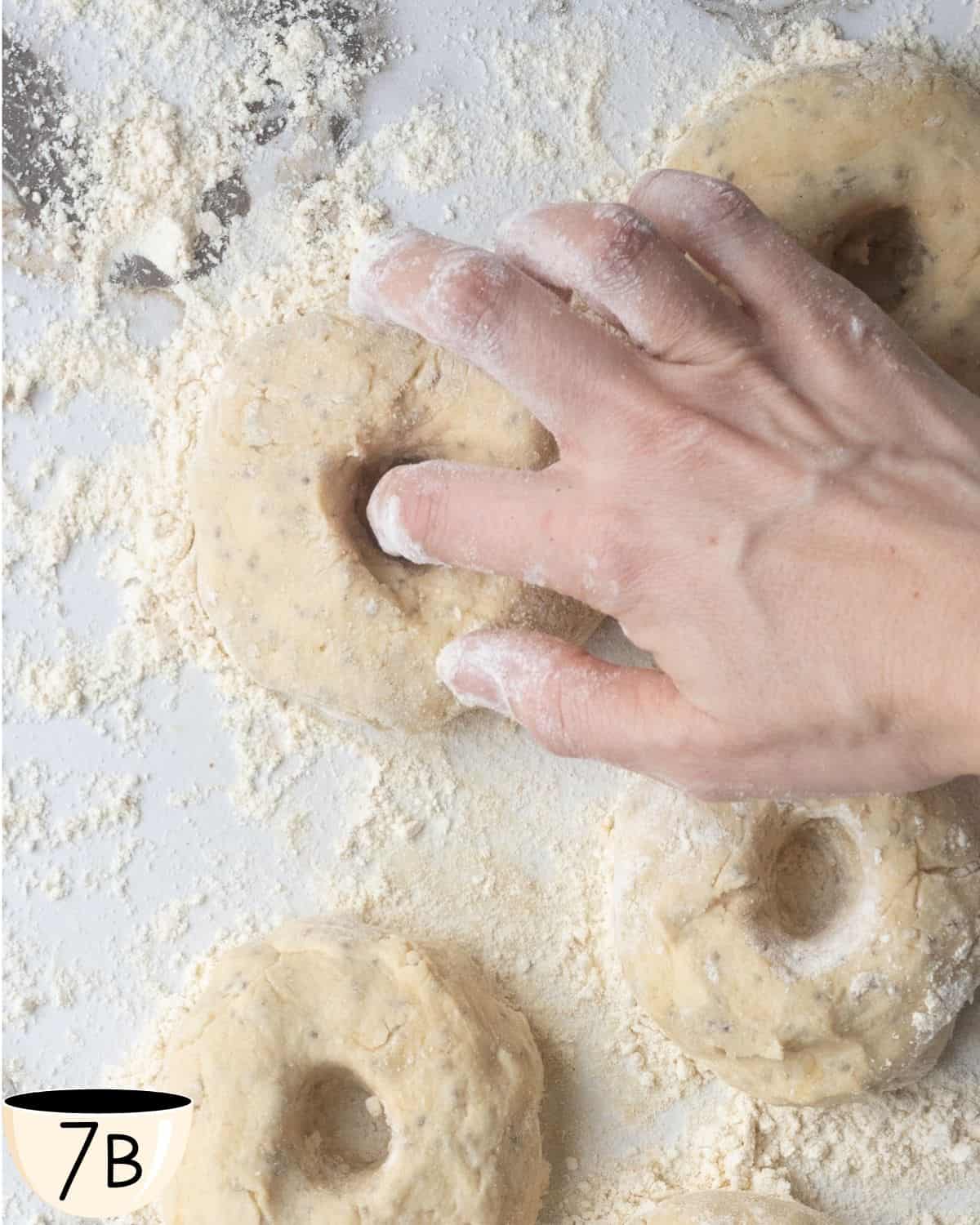 Hand forming a hole in the center of a gluten-free vegan bagel dough ball on a floured surface.