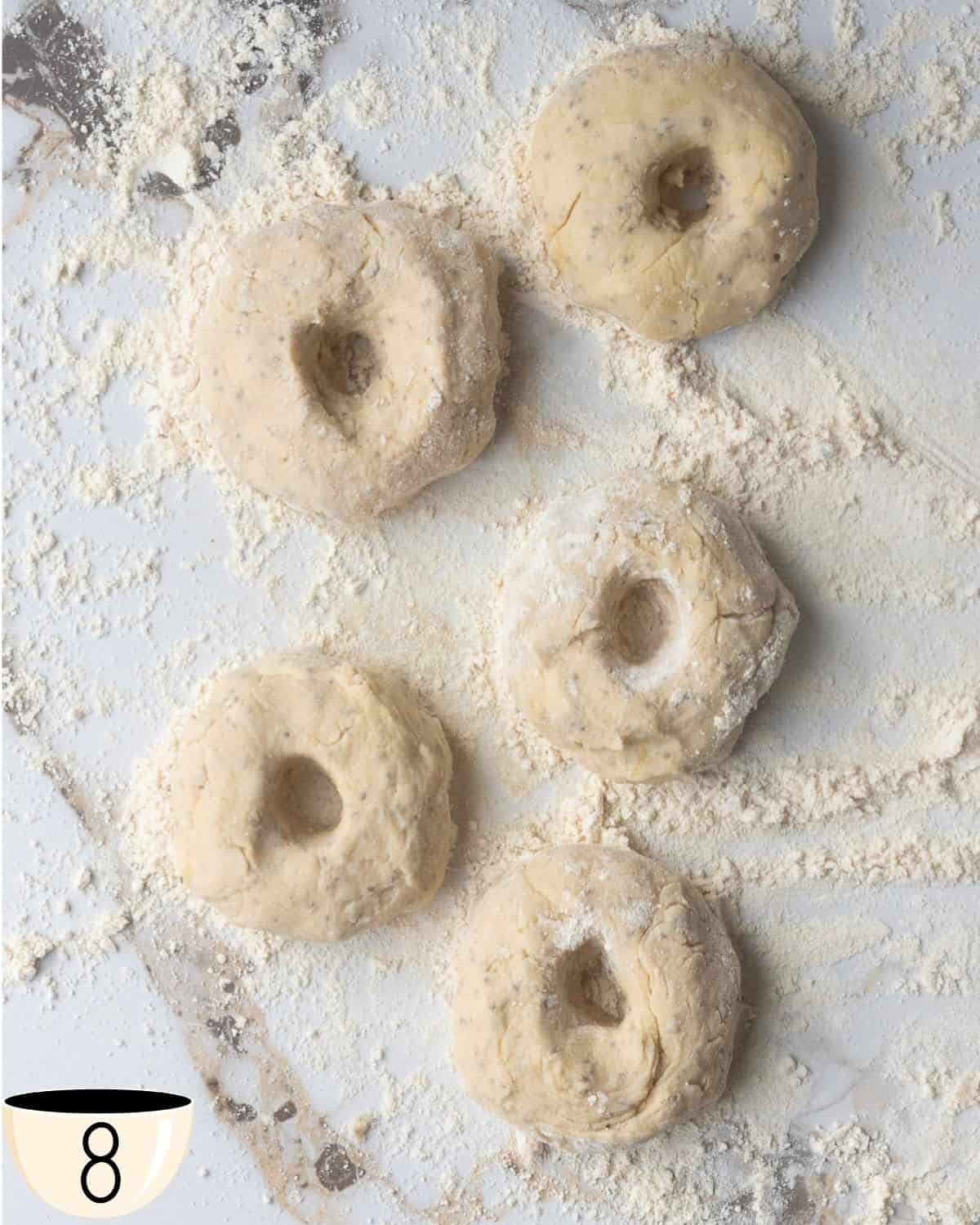 Four shaped gluten-free vegan bagels on a floured marble surface.