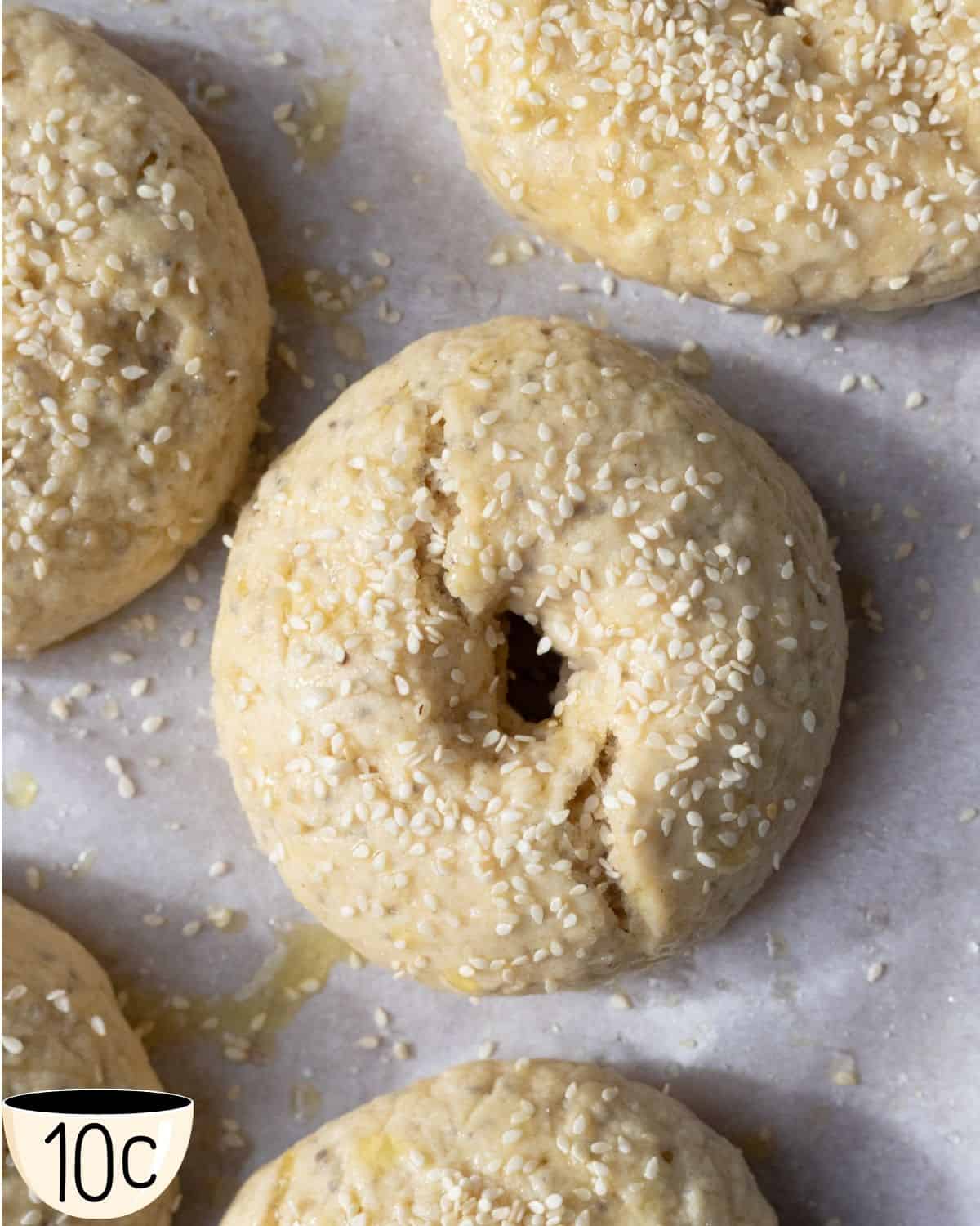 Gluten-free vegan bagels on parchment paper sprinkled with sesame seeds, ready for baking.