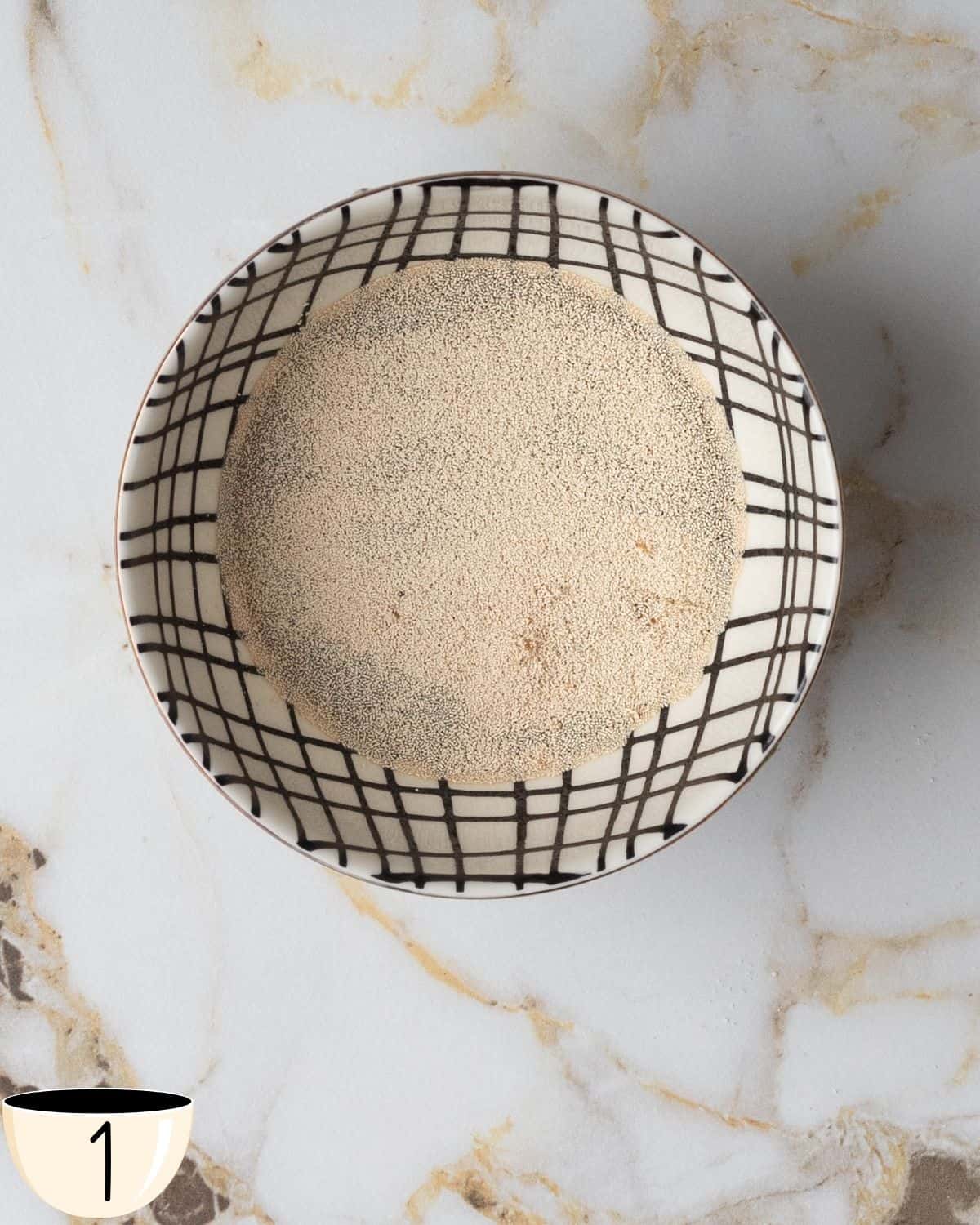 Close-up of a small bowl of instant yeast on a marble surface.