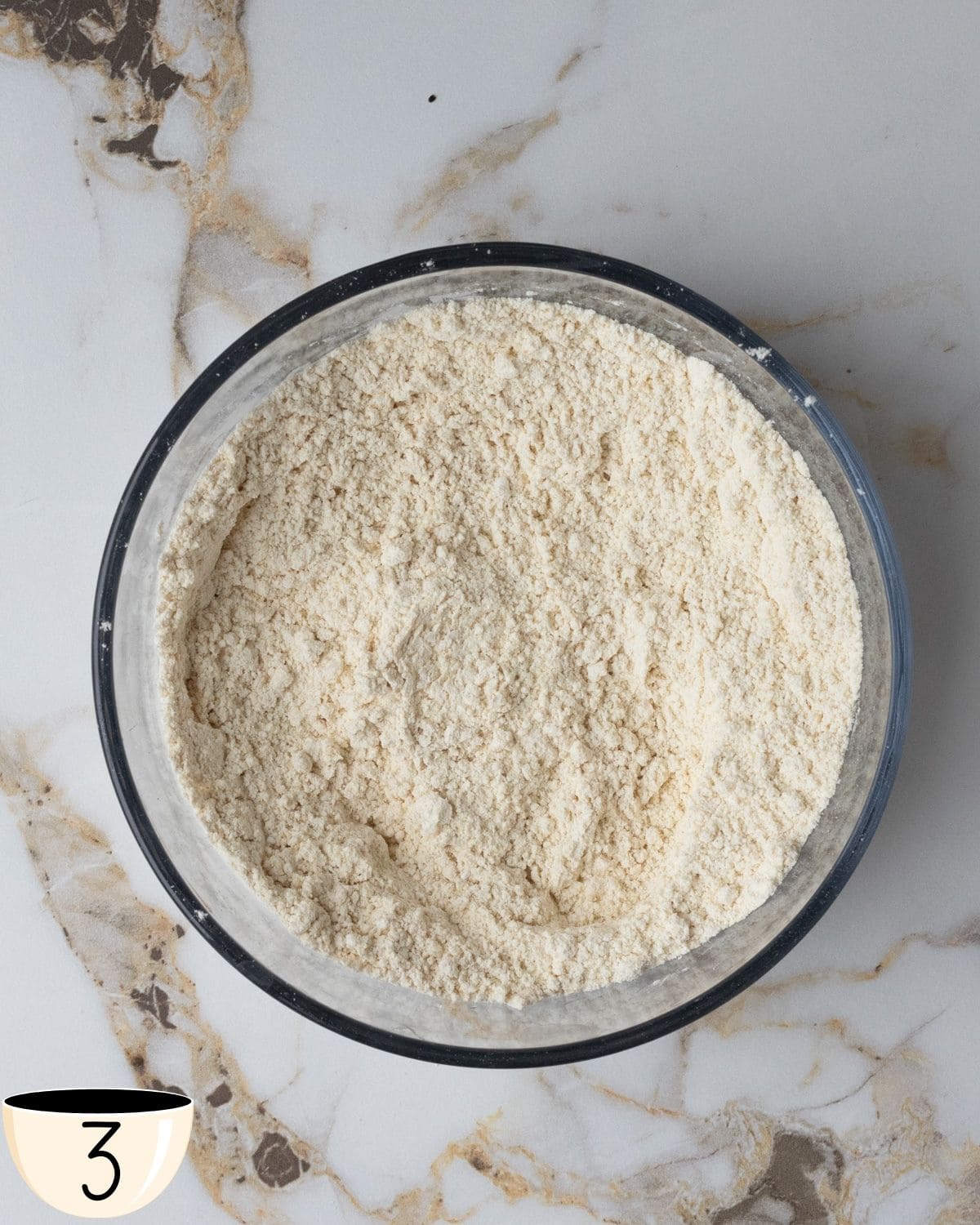 A large bowl of gluten-free all-purpose flour mixed with baking powder, and salt on a marble countertop.