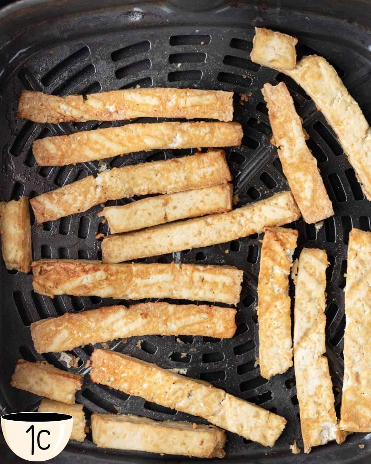 Cooked tofu strips in an air fryer tray, golden and crispy after air frying.