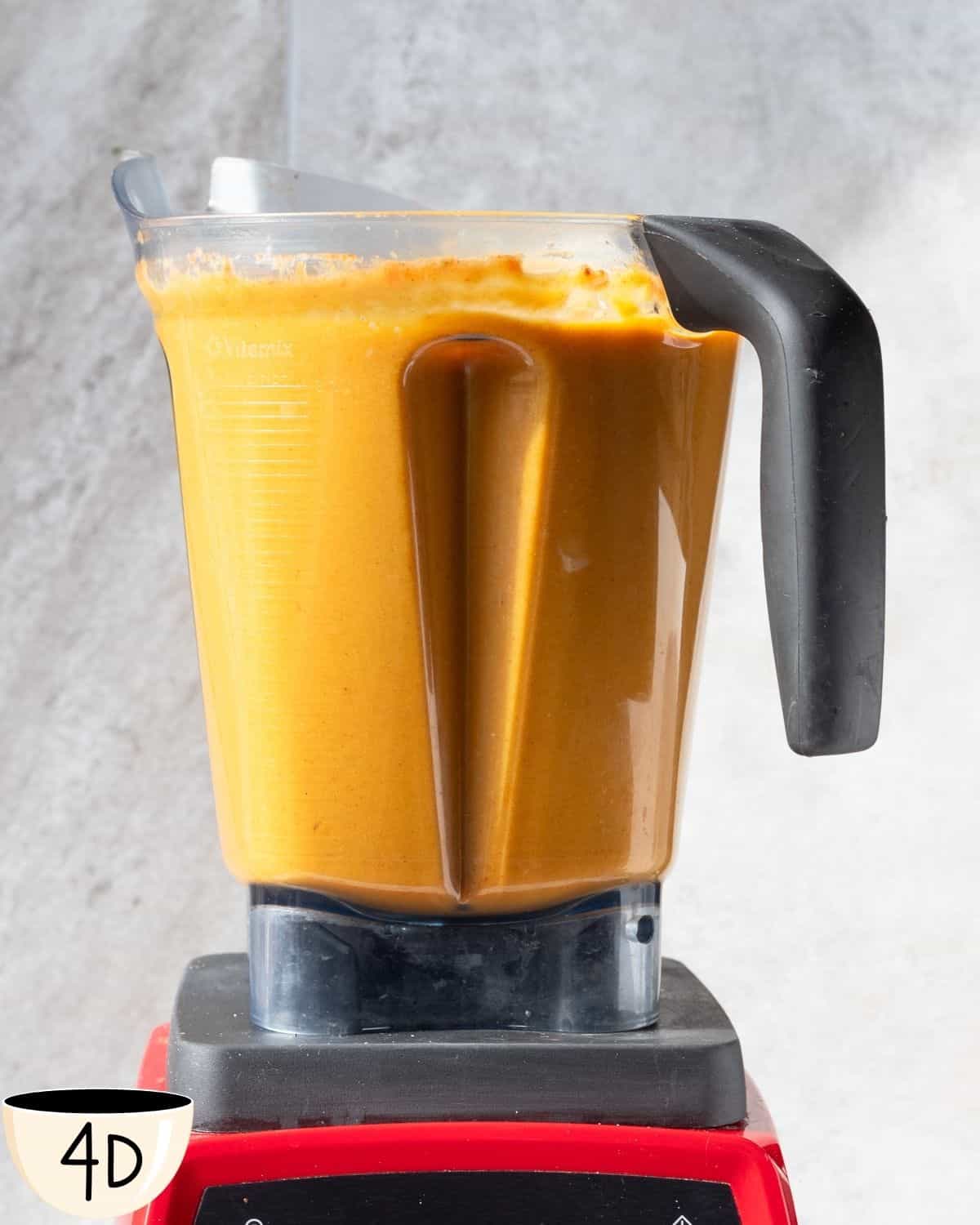 A Vitamix blender filled to the brim with a smooth, orange-colored roasted pumpkin and cauliflower soup, ready to be served.