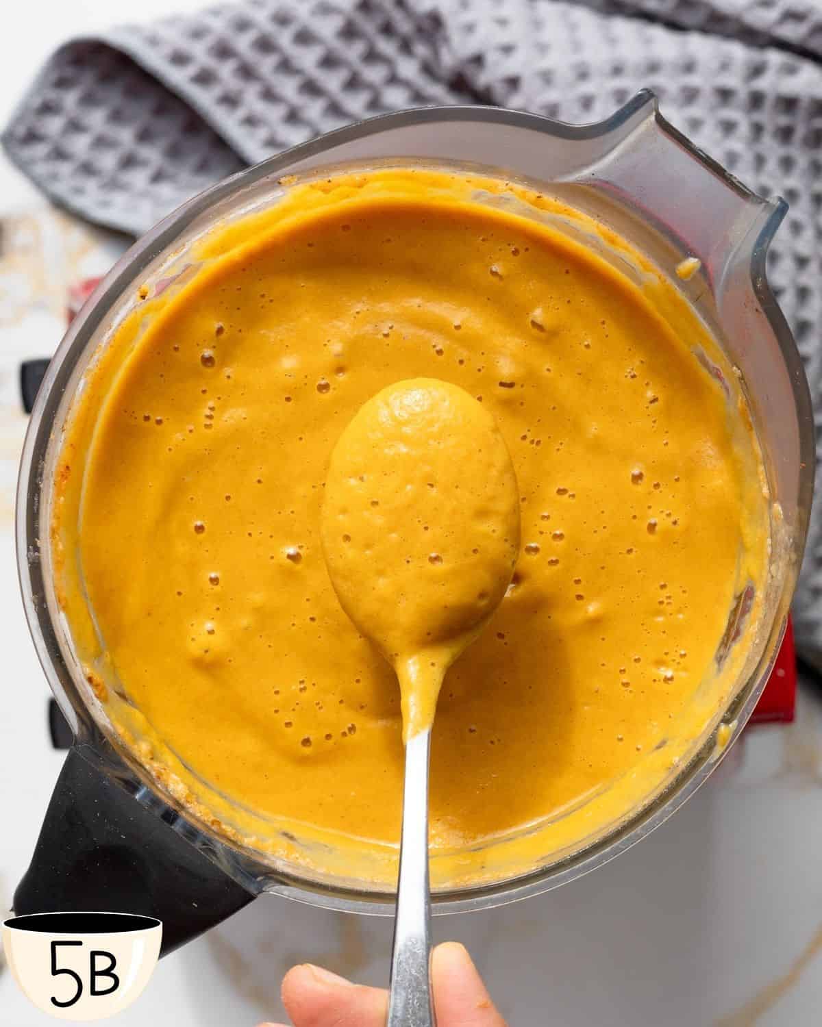 Overhead shot of a high-speed blender filled with ingredients for pumpkin and cauliflower soup, including a spoon for tasting.