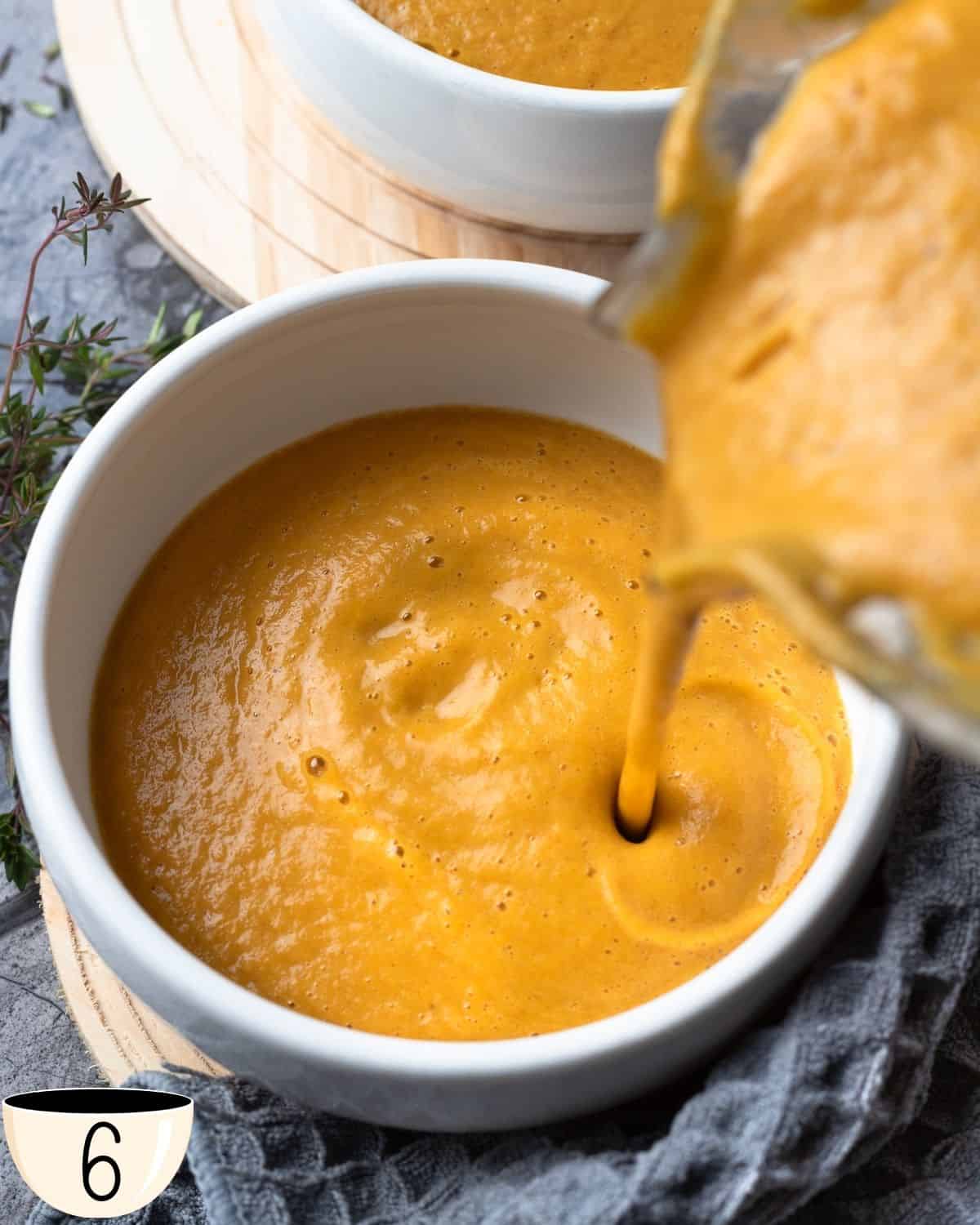 Freshly blended pumpkin and cauliflower soup being poured into a white bowl, highlighting its smooth consistency.