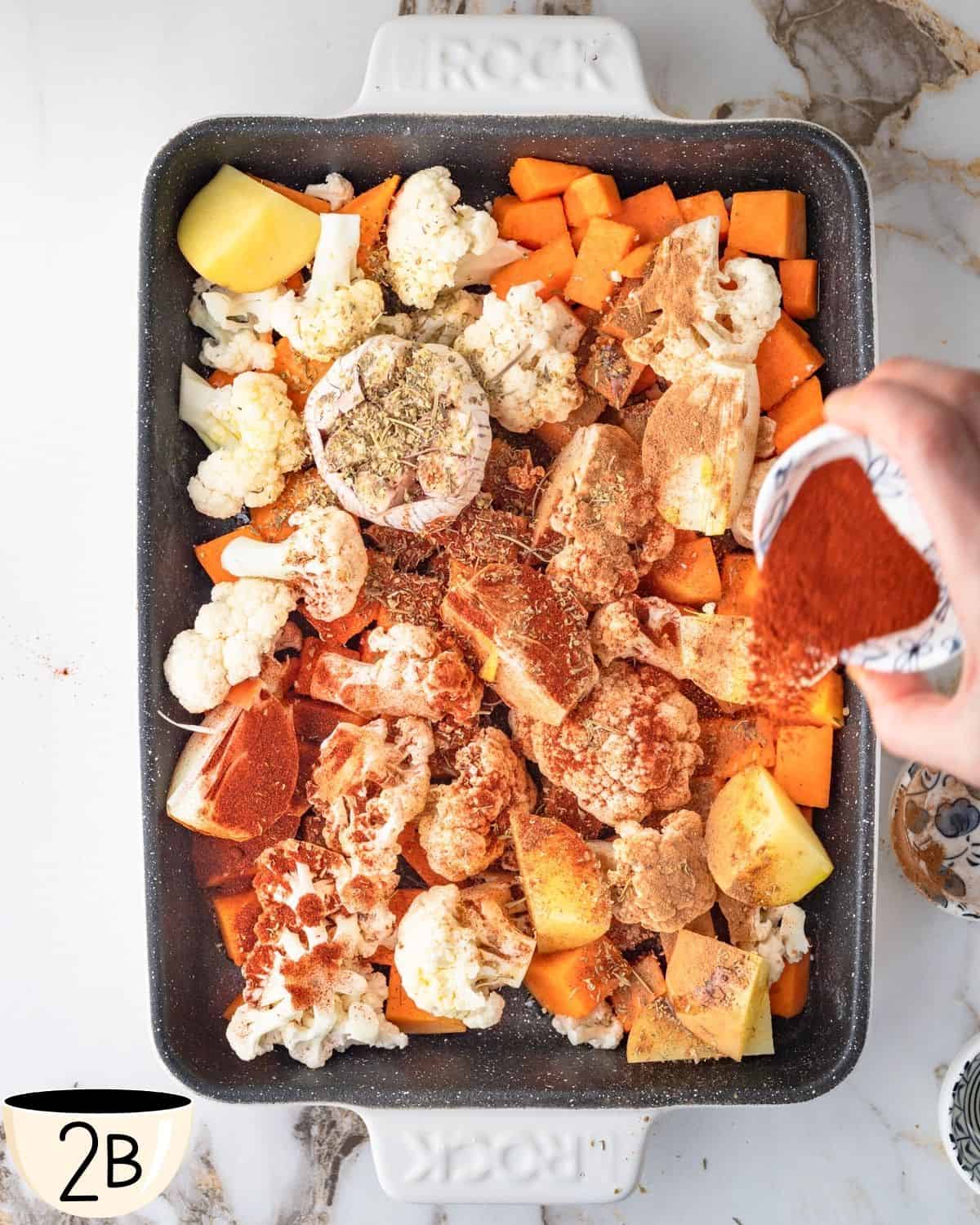 A baking tray with chopped pumpkin, cauliflower, and potatoes dusted with various spices in preparation for roasting.