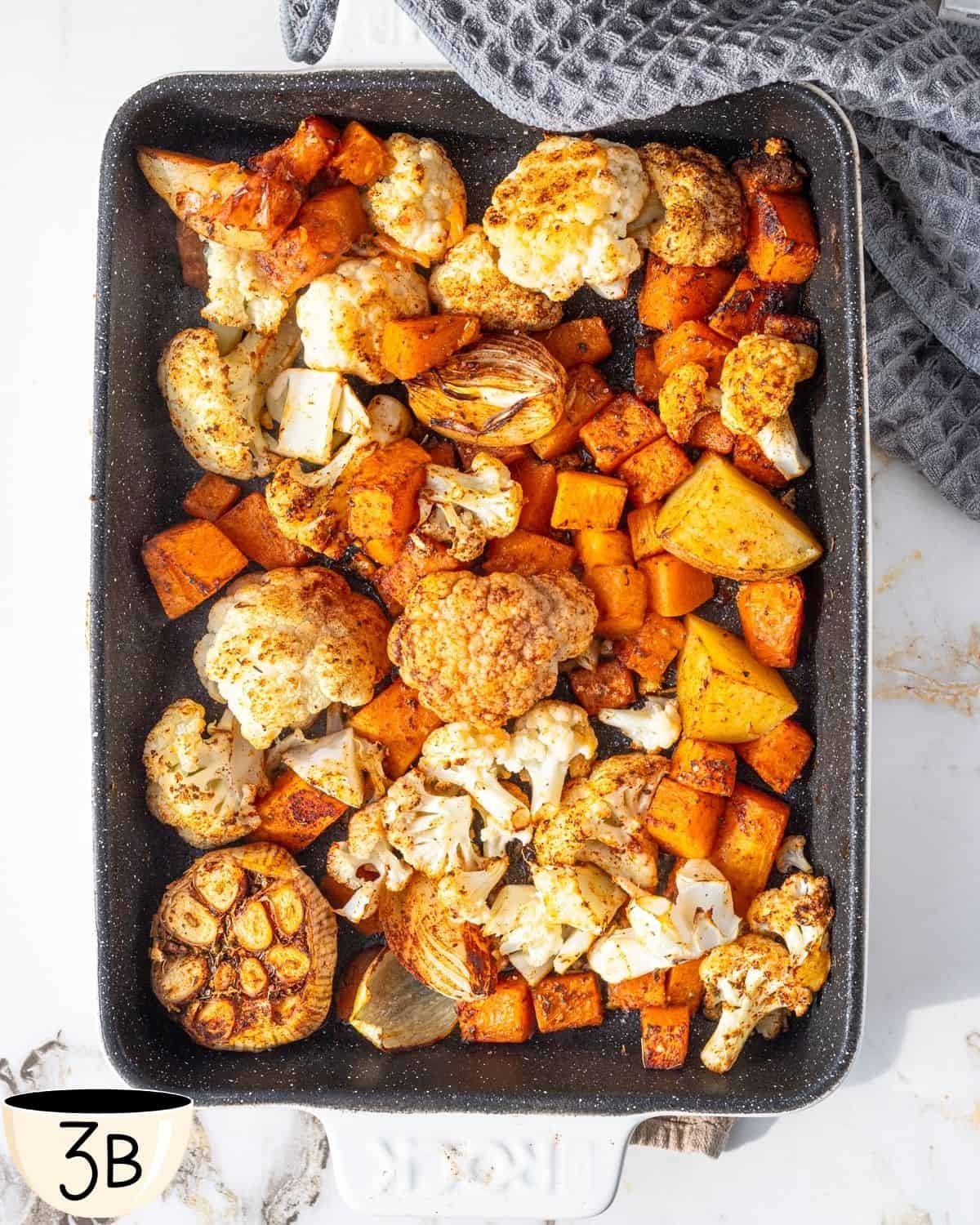 A high-angle shot of a baking tray with well-roasted pumpkin and cauliflower, edges caramelized, ready for the next step in the recipe.