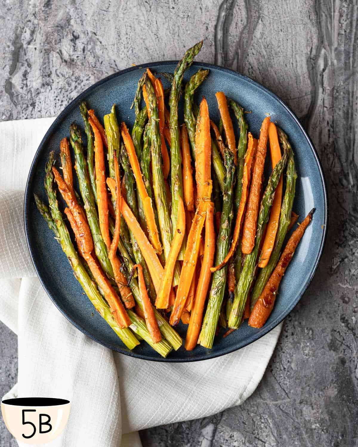 A serving of roasted veggies on a dark blue plate, set on a gray stone countertop with a linen napkin.