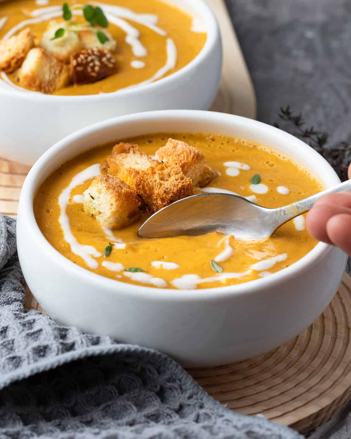 A creamy bowl of pumpkin and cauliflower soup garnished with a drizzle of cream and croutons, ready to be enjoyed.