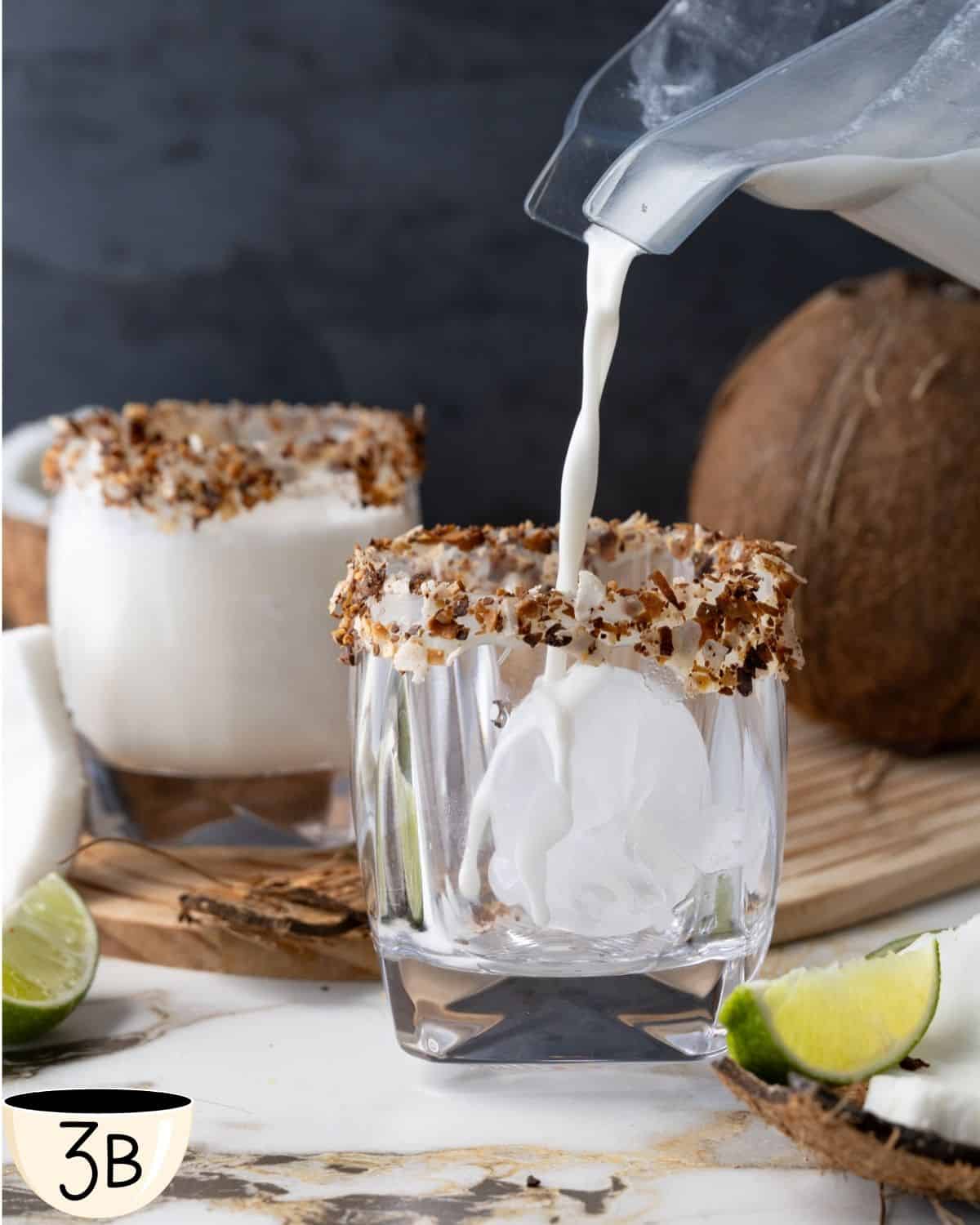 Pouring the batida de coco mixture from a blender into a glass filled with ice cubes.