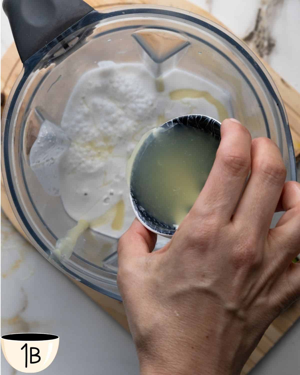 Hand pouring lime juice into a blender with coconut milk and condensed coconut milk.